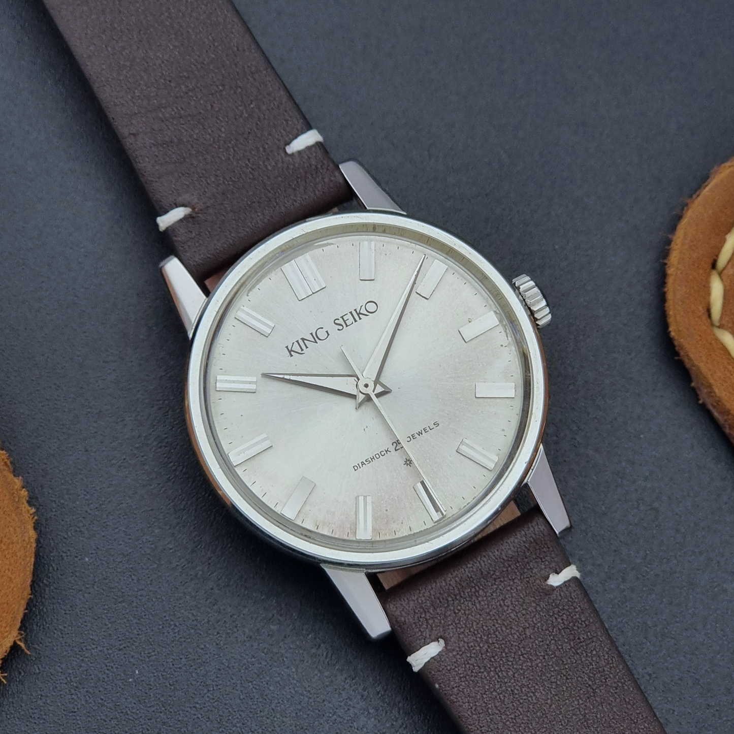 Vintage King Seiko J14102E Wristwatch with brown leather strap on a dark gray background close up dial