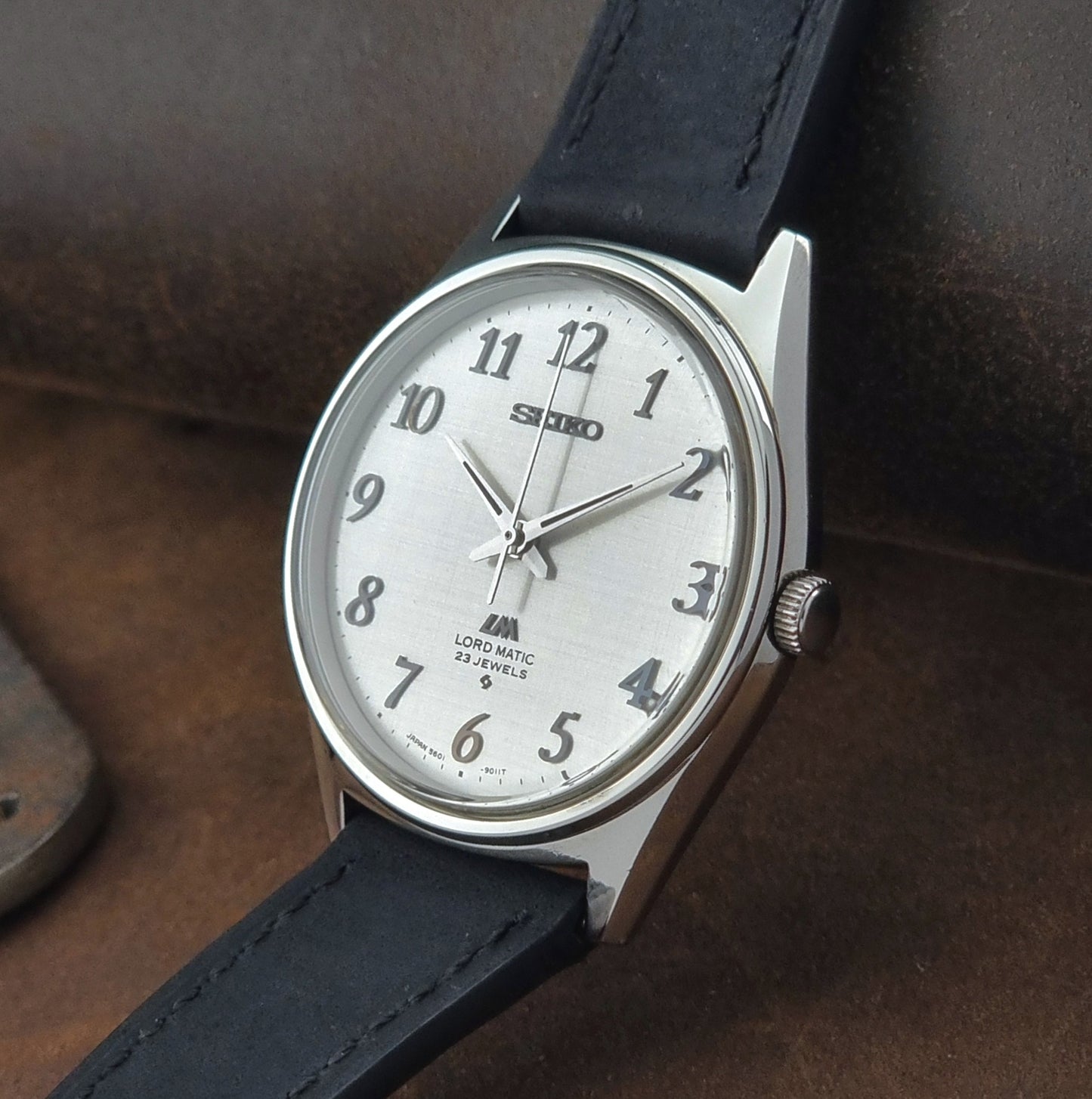 Seiko watch with black leather strap on a brown textured background