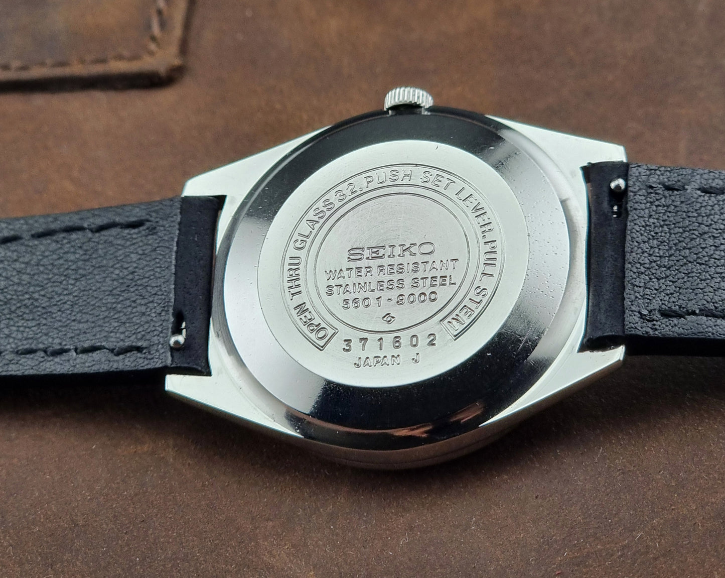 Seiko watch back with branding and model number on a brown leather background