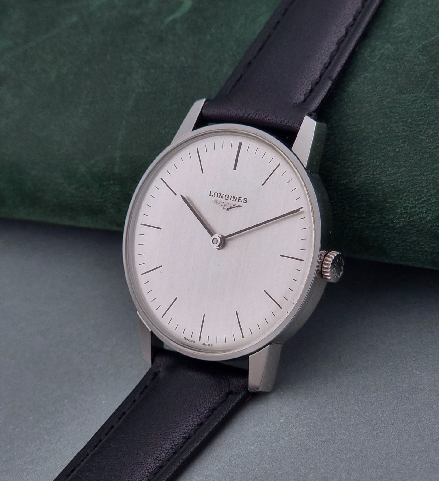 Vintage Longines watch with black leather strap on a green surface