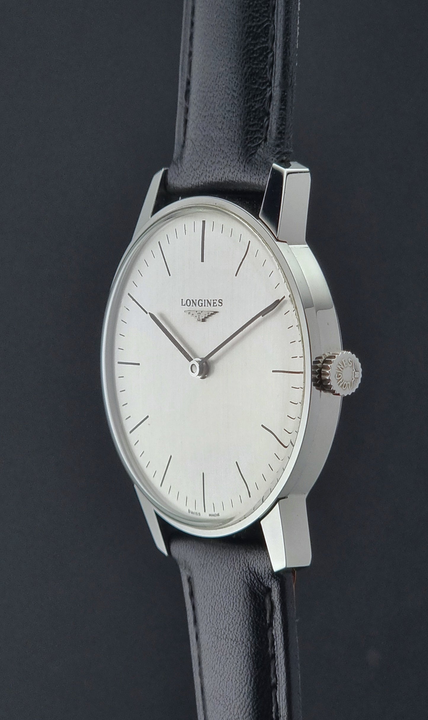 Vintage Longines watch with black leather strap on a grey surface