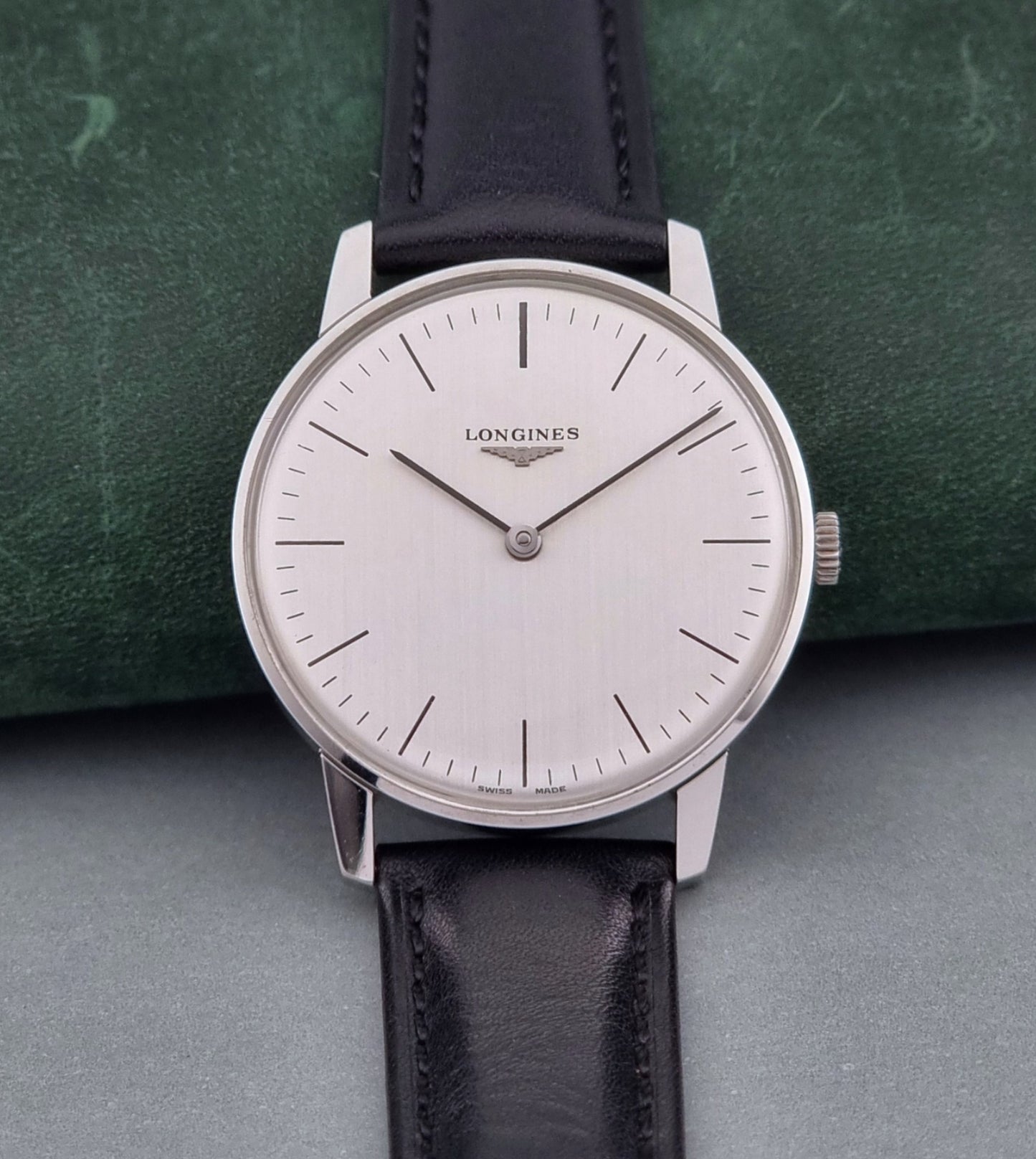 Vintage Longines watch with black leather strap on a green surface