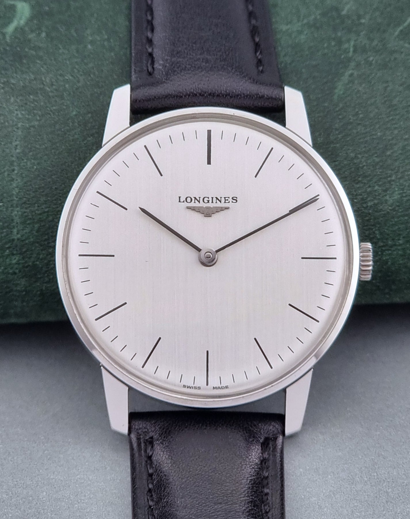 Vintage Longines watch with black leather strap on a green surface