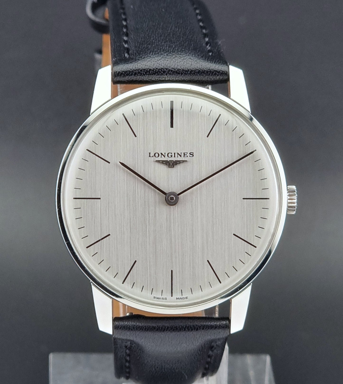Vintage Longines watch with black leather strap on a green surface