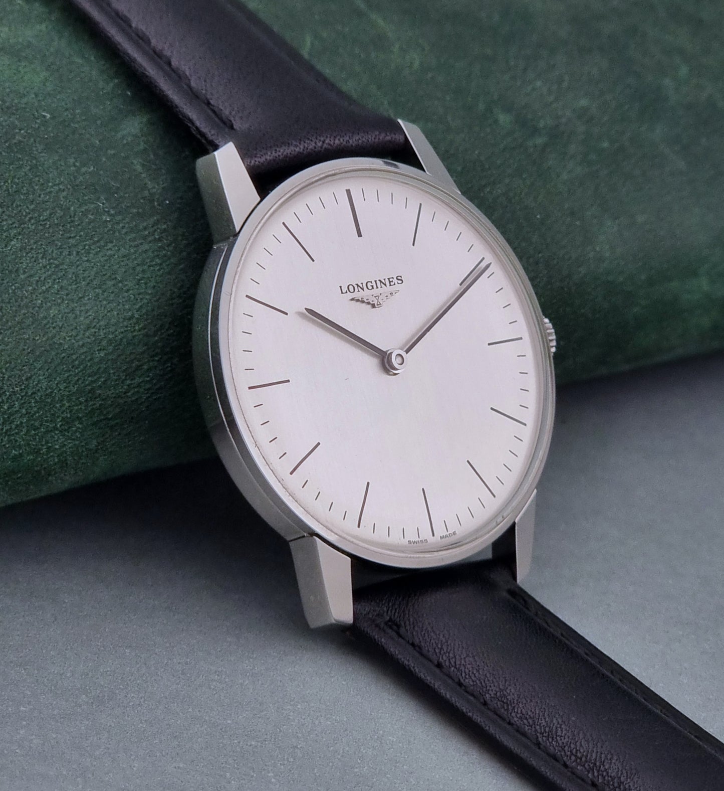Vintage Longines watch with black leather strap on a green surface