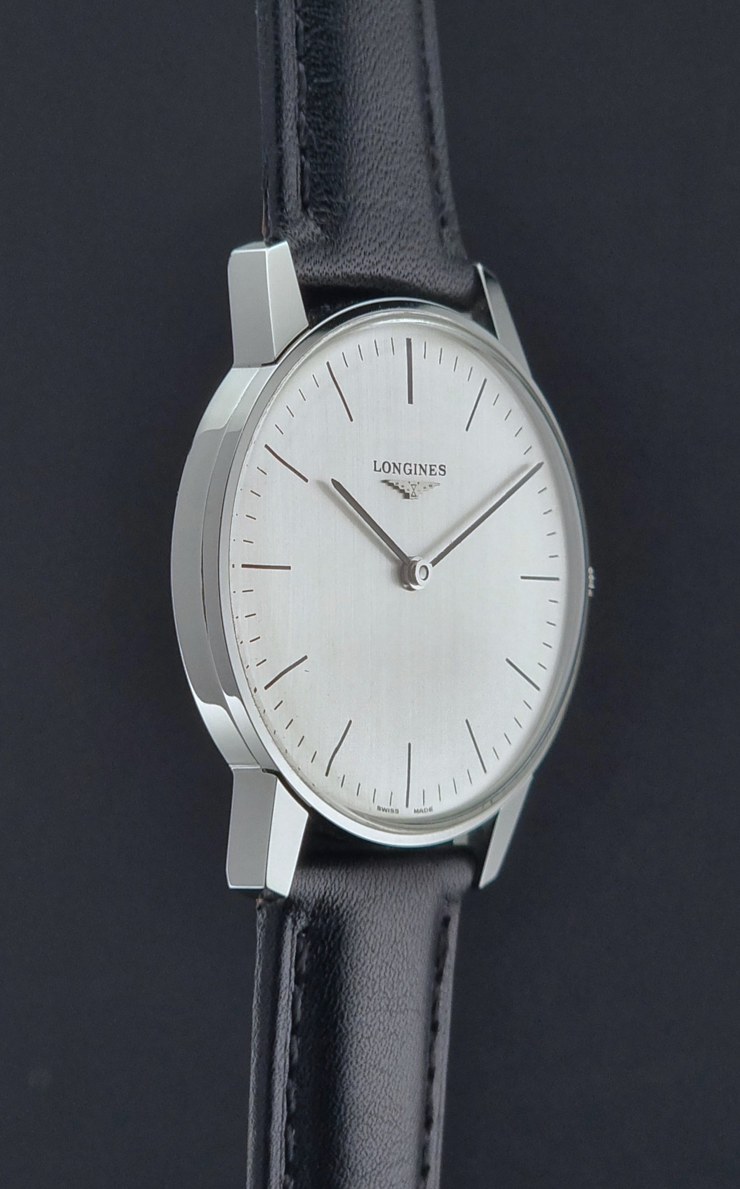 Vintage Longines watch with black leather strap on a grey surface