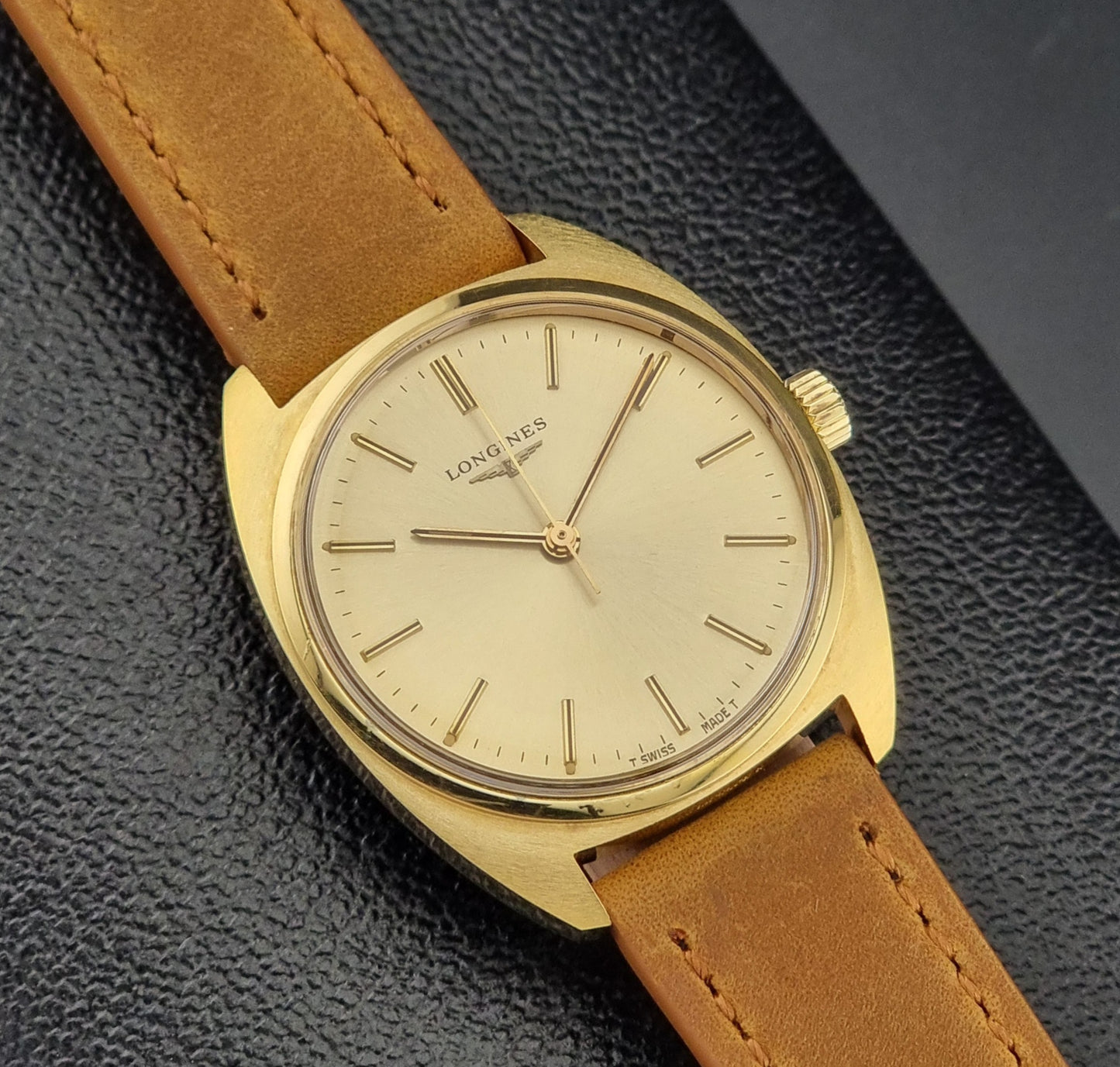 Vintage Gold Longines wristwatch with brown leather strap on a dark textured background