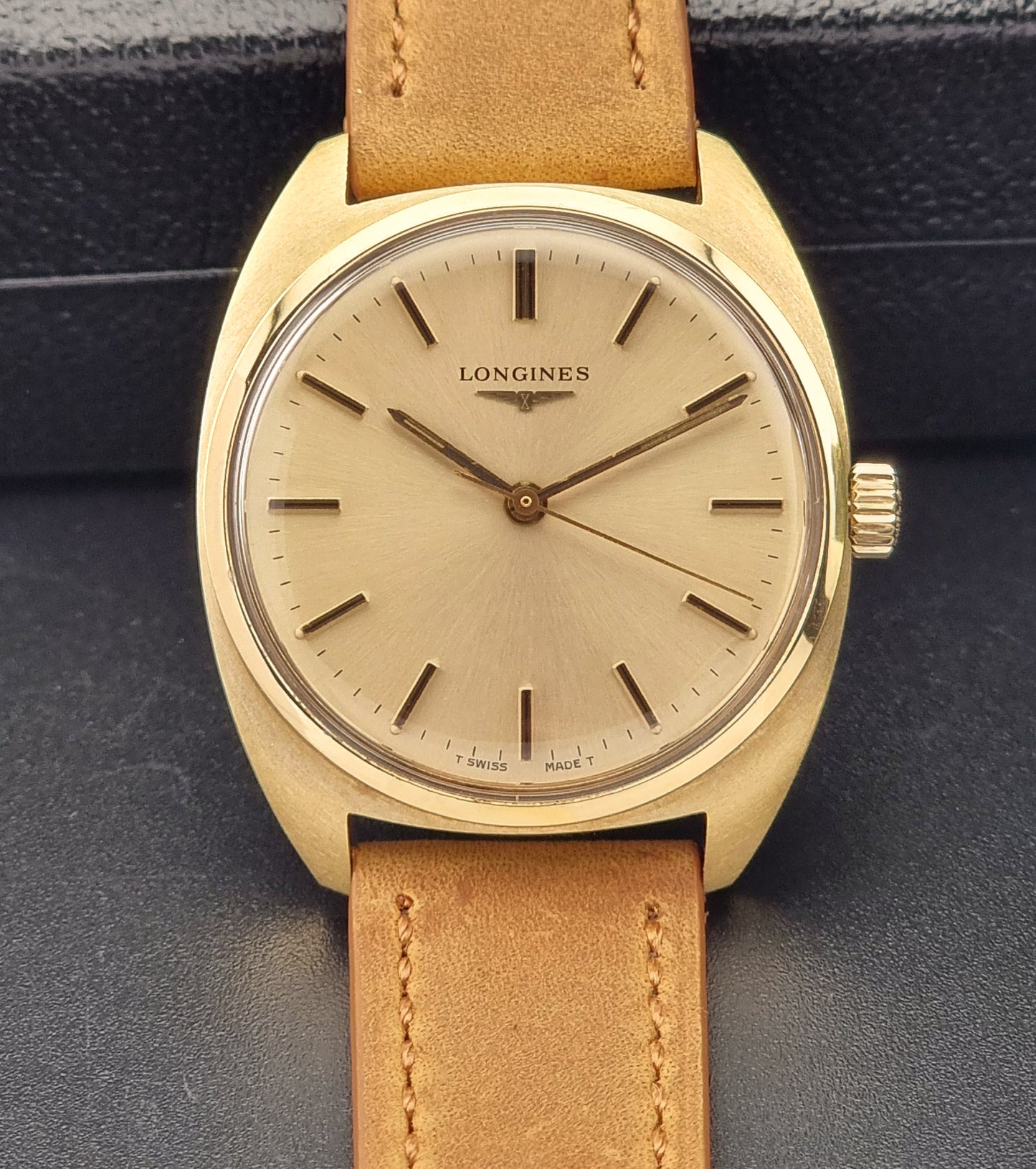 Front View of a Longines watch with gold case and brown leather strap on a dark background