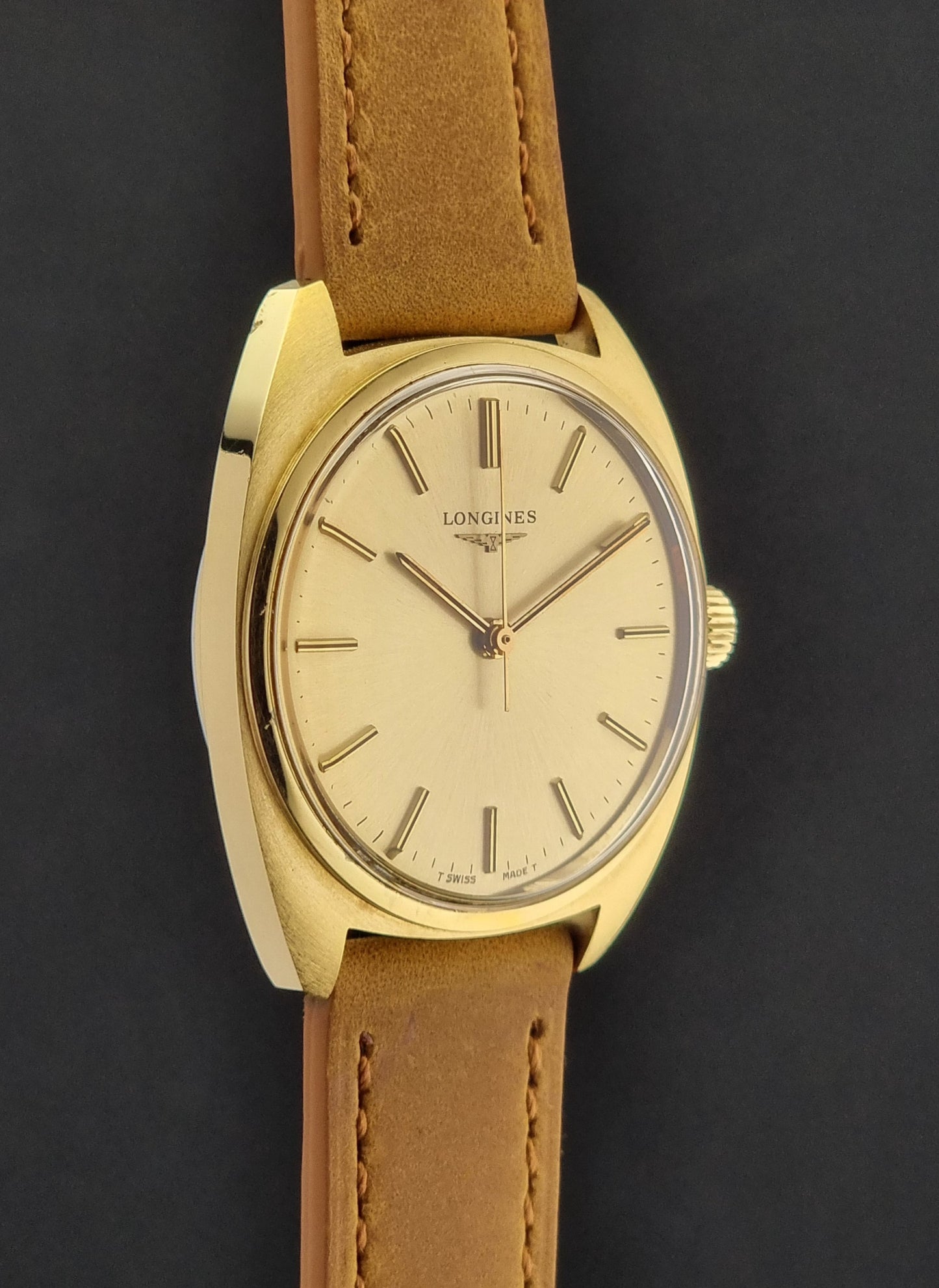 Side View of a Vintage Gold Longines wristwatch with brown leather strap on a dark background
