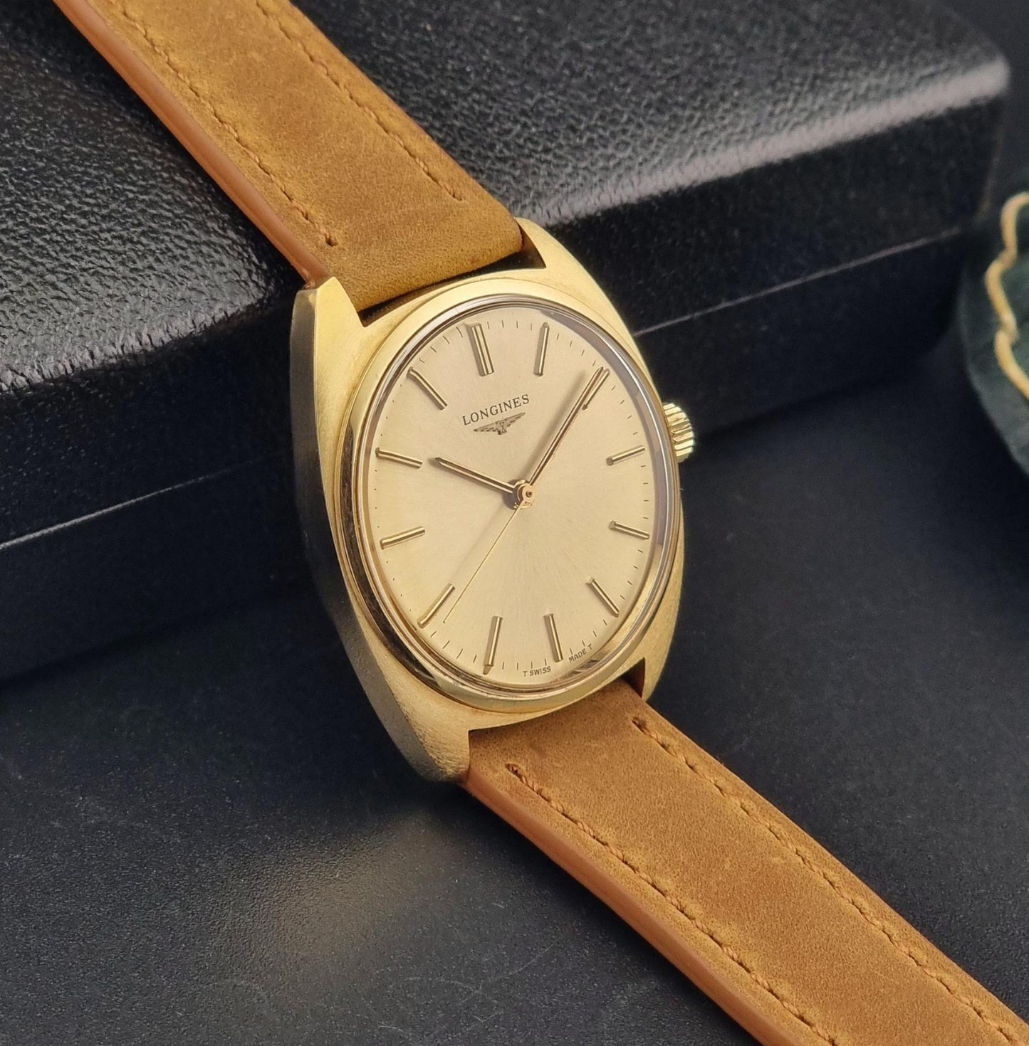 Vintage Gold Longines wristwatch with brown leather strap on a dark surface