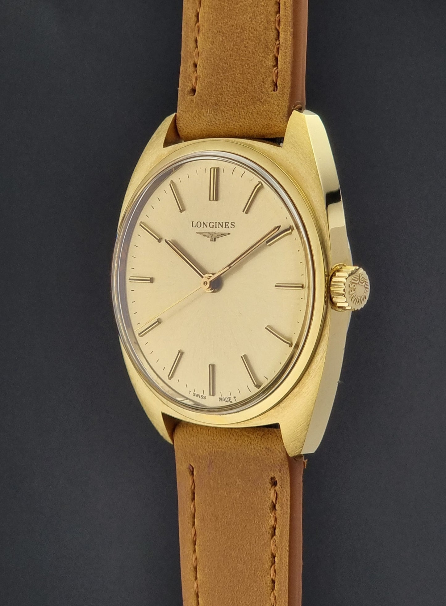 Side view of a Vintage Gold Longines watch with a brown leather strap on a dark background