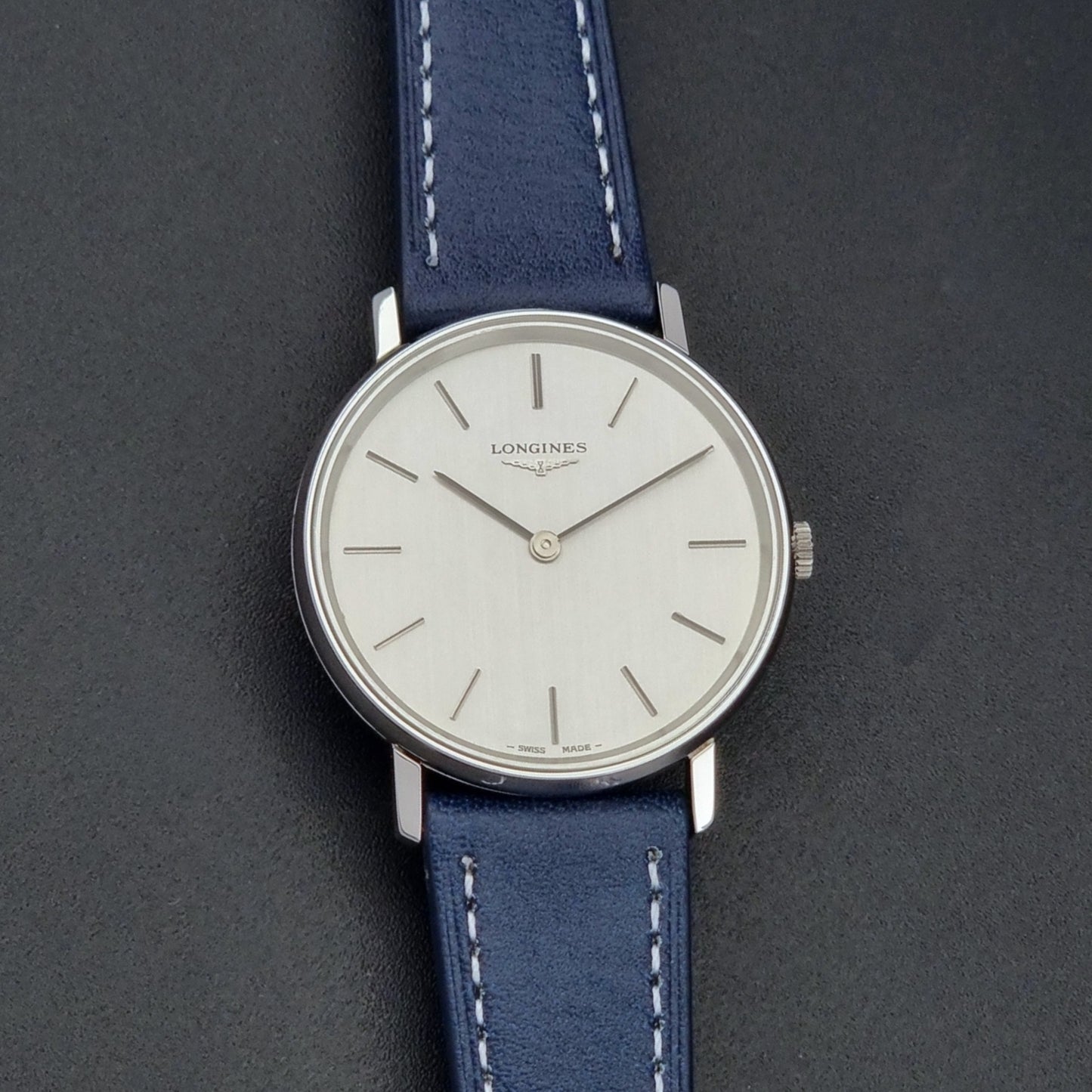 Vintage Longines Wristwatch 4127 with blue strap and silver case on a dark gray background front view