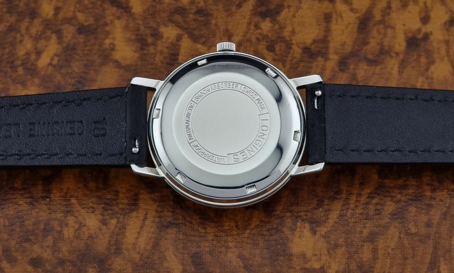 Back view of a Vintage Longines Flagship watch with a black leather strap on a wooden surface