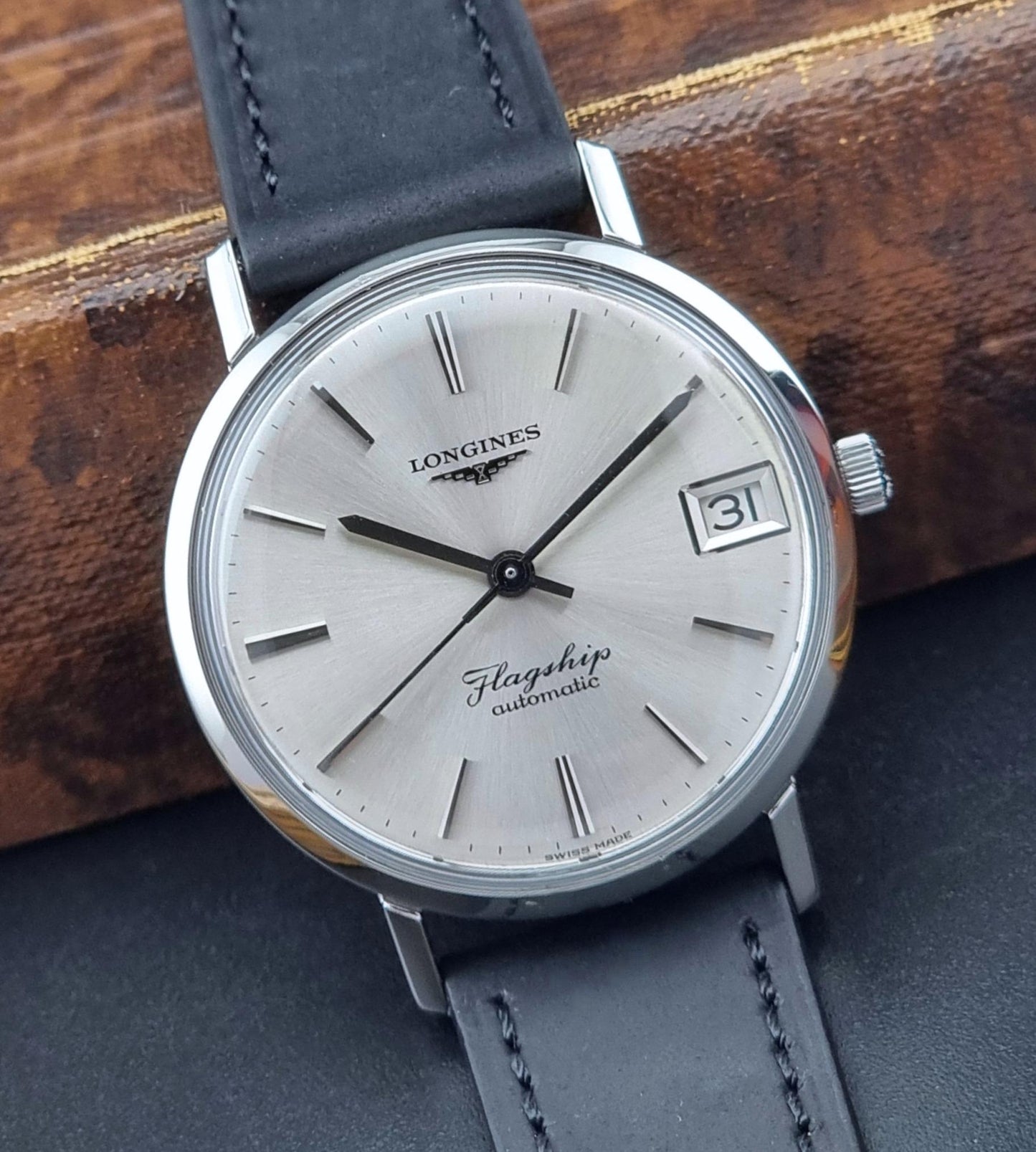 Longines watch with silver dial and black leather strap on a wooden surface