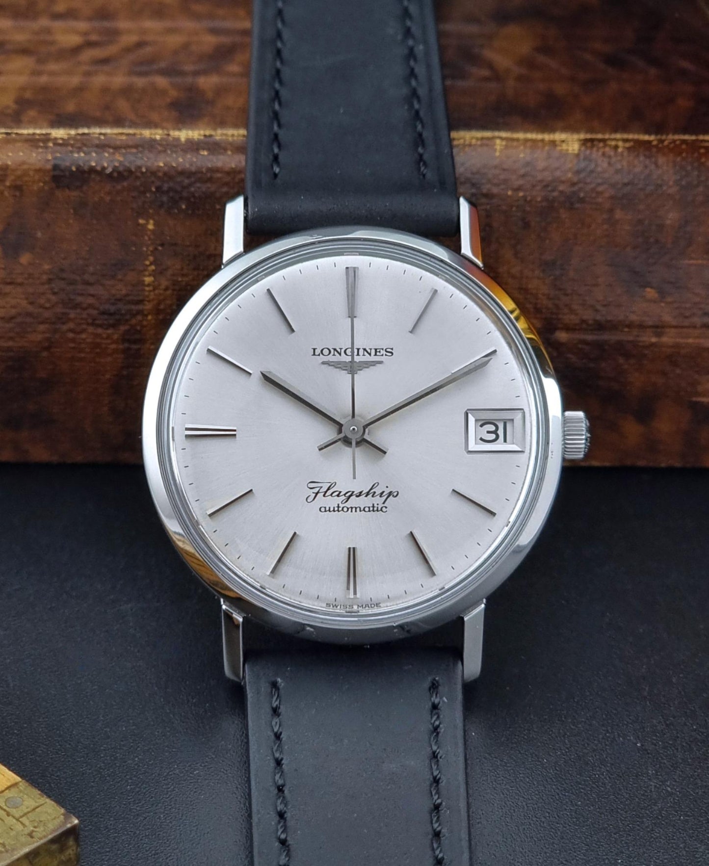 Front view of a Vintage Longines Flagship watch with silver dial and black leather strap on a dark surface