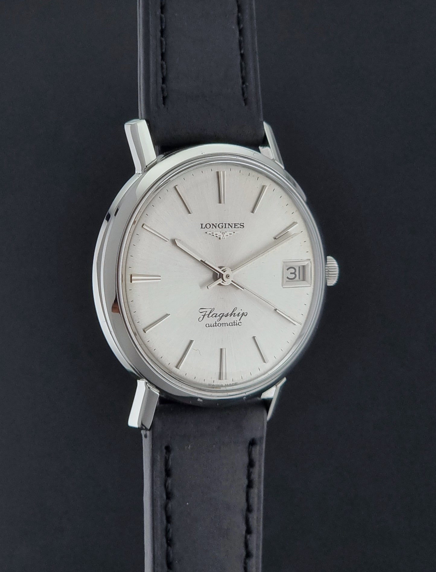 Vintage Longines Flagship watch with silver dial and black leather strap on a dark background