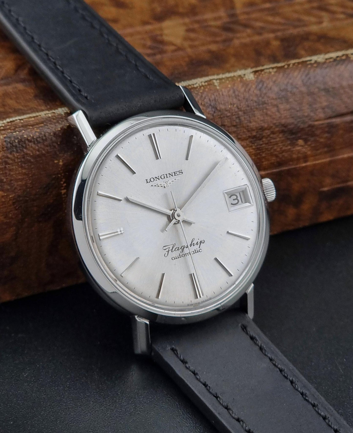 Vintage Longines Flagship watch with black leather strap on a wooden surface