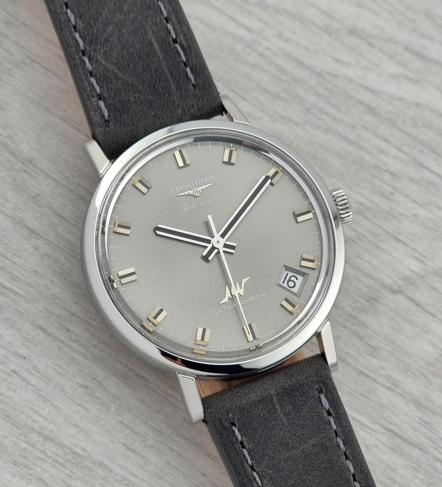Vintage Longines Ultra-Chron Watch with gray dial and black leather strap on a textured surface