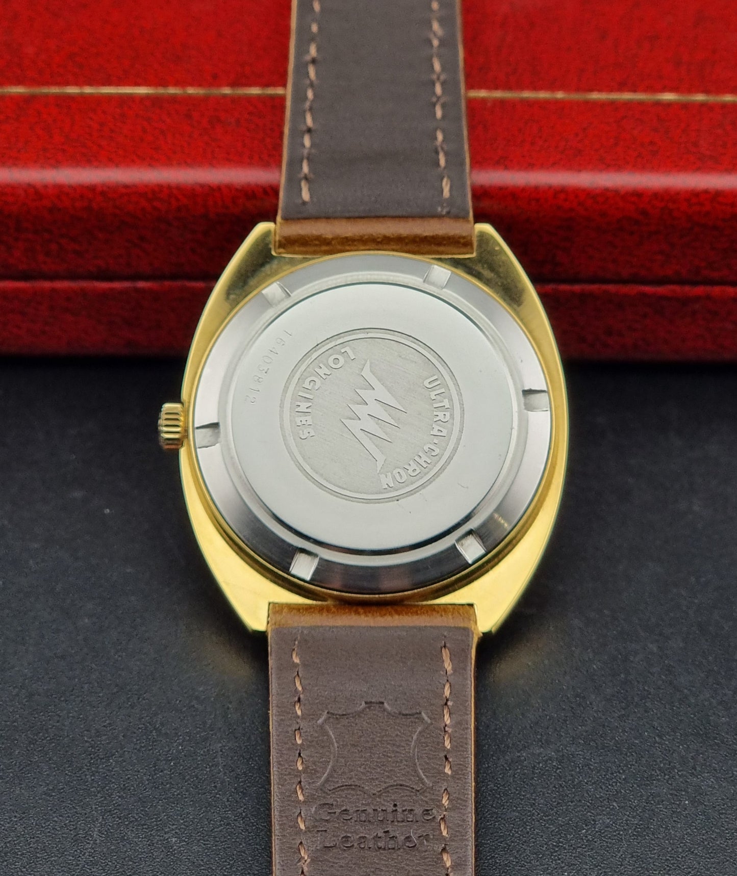 Vintage Longines Gold watch case back with brown leather strap on a dark surface with red background