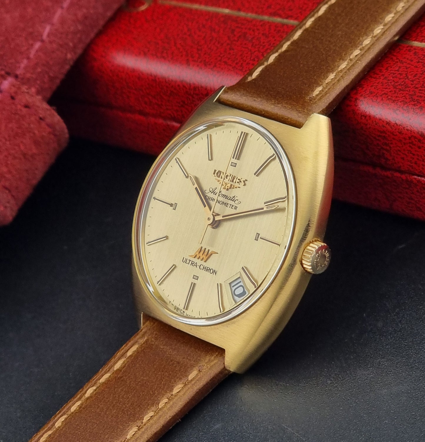 Vintage Longines Gold wristwatch with brown leather strap on a dark surface with red background