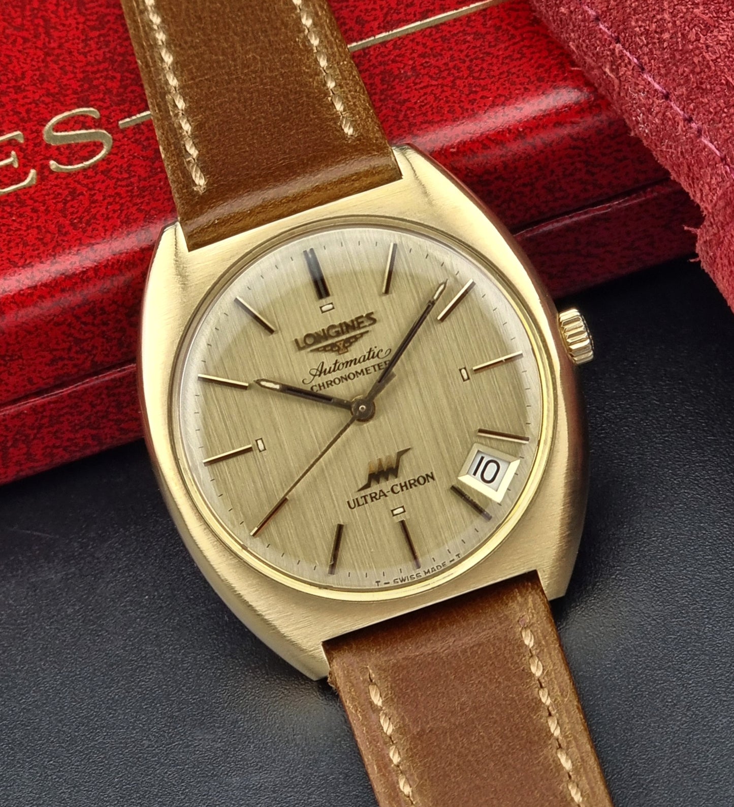 Vintage Longines Gold watch with brown leather strap on a dark surface with a red box in the background