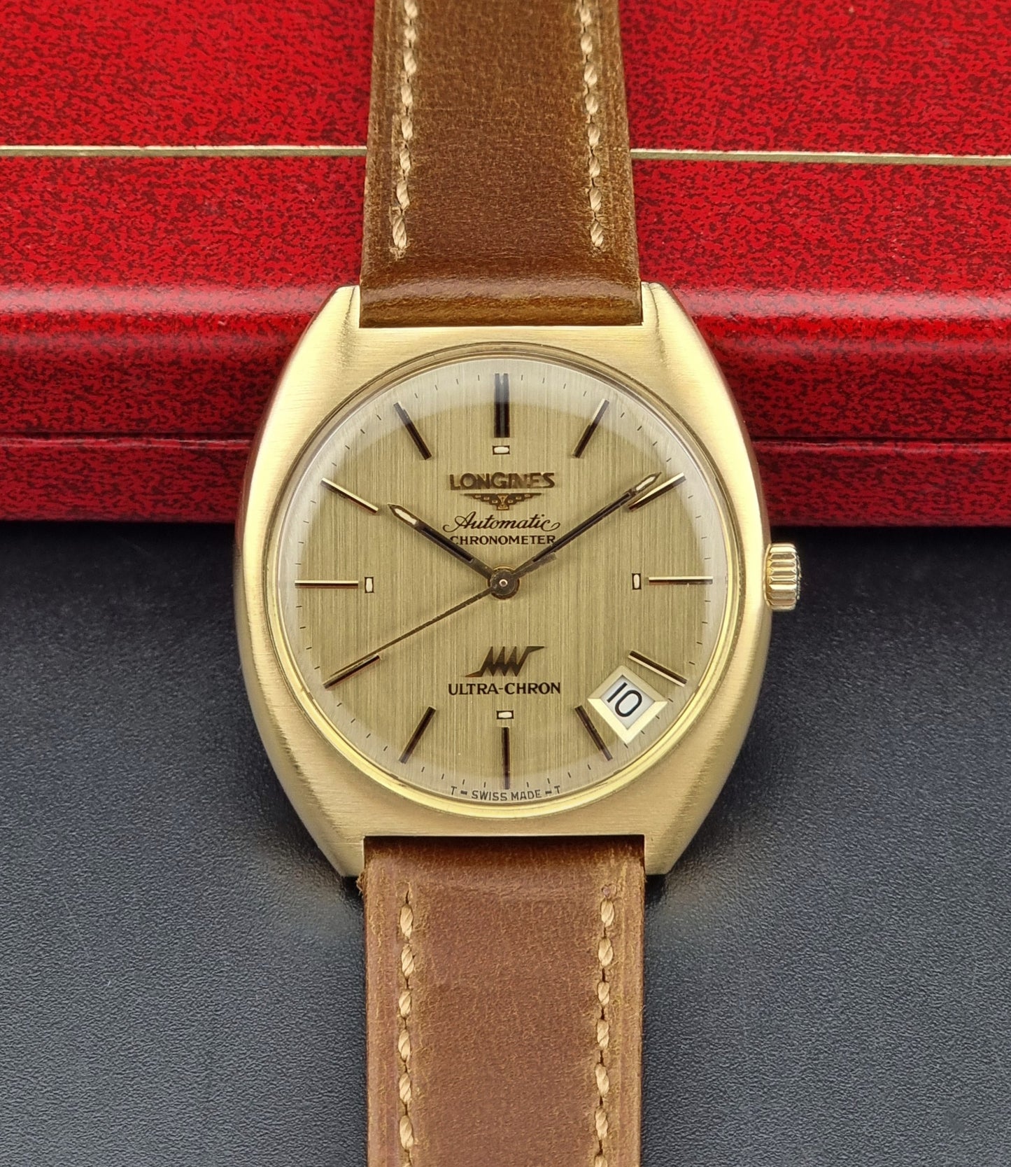 Vintage Longines Gold wristwatch with brown leather strap on a red and gray background
