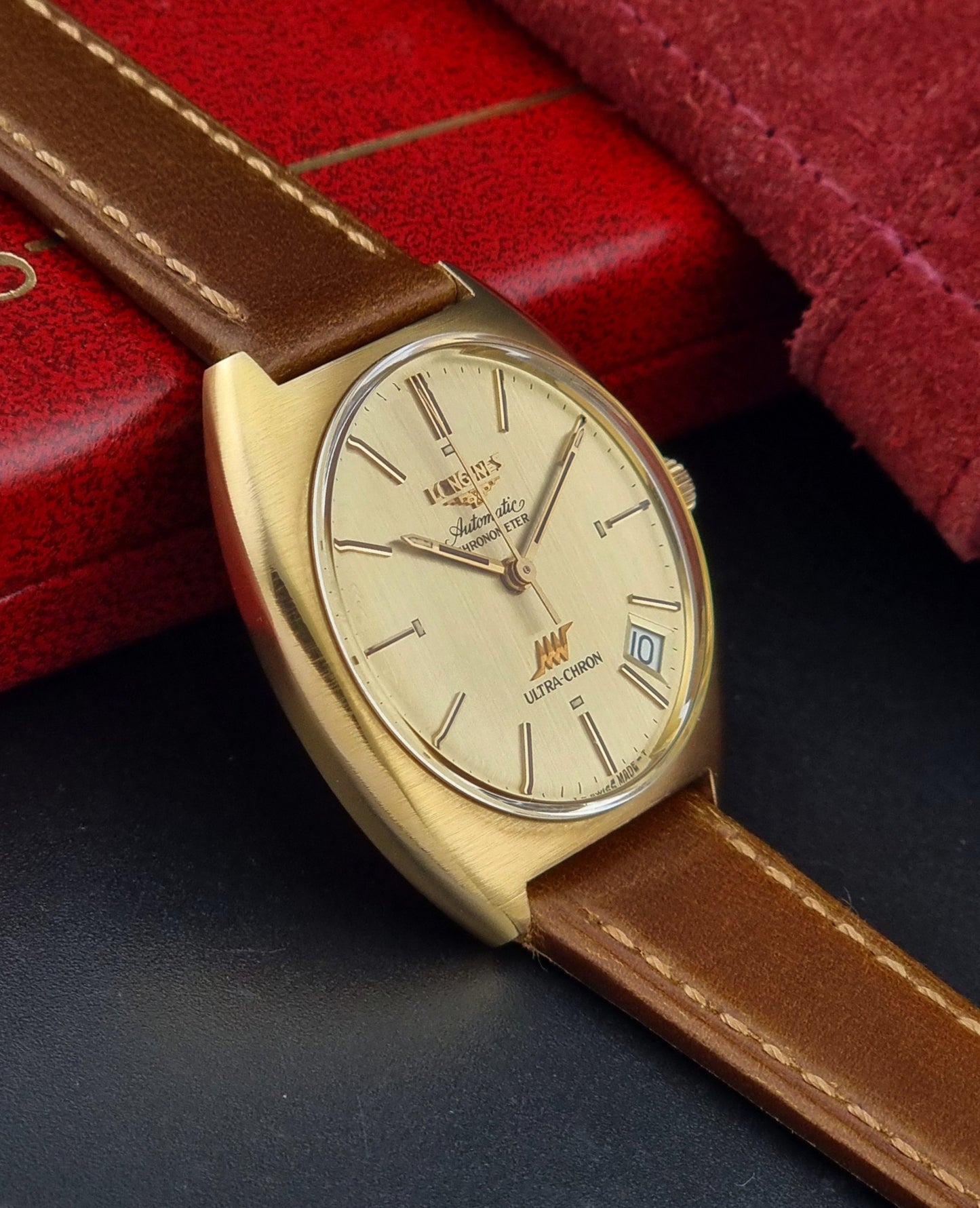 Vintage Longines Gold wristwatch with brown leather strap on a dark surface