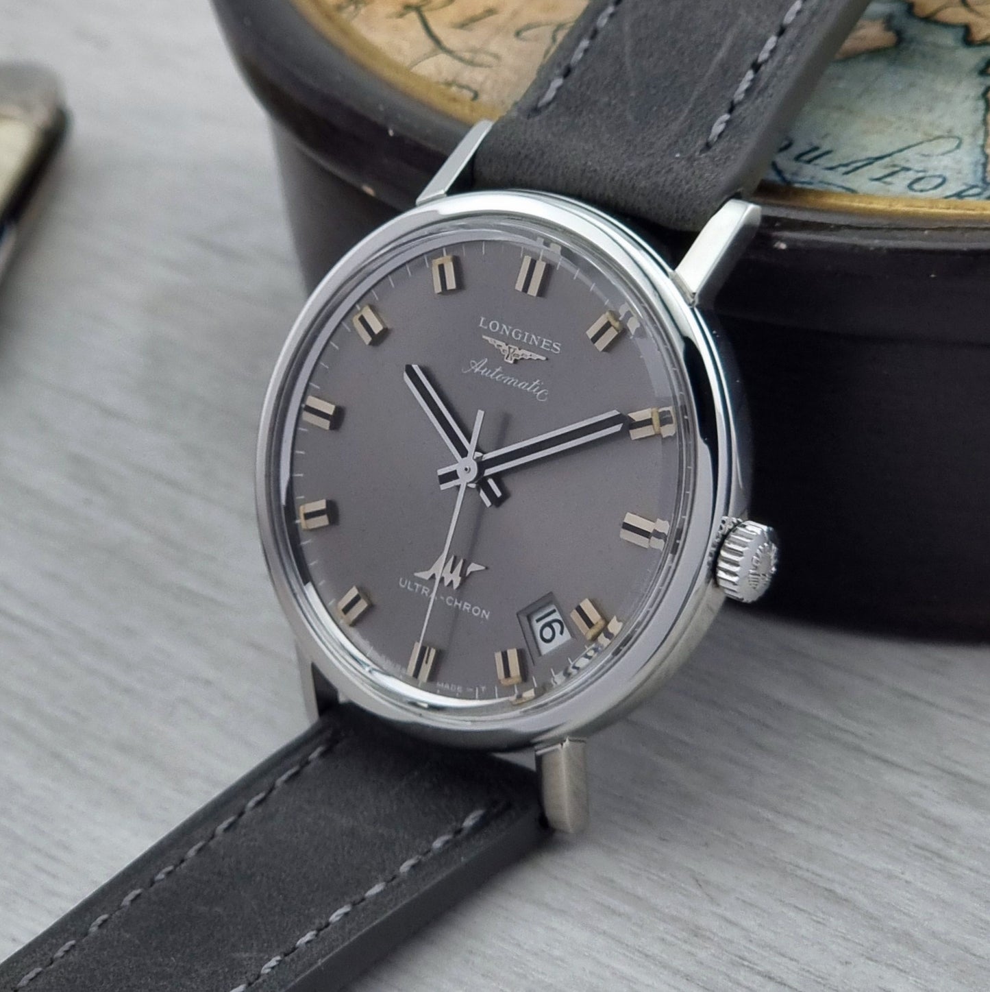 Luxury Vintage Longines Ultra-Chron watch with gray dial and black leather strap on a textured surface