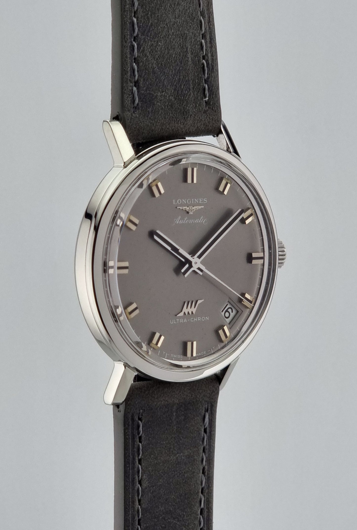 Vintage Longines Ultra-Chron Wristwatch with gray dial and black leather strap on a light gray background