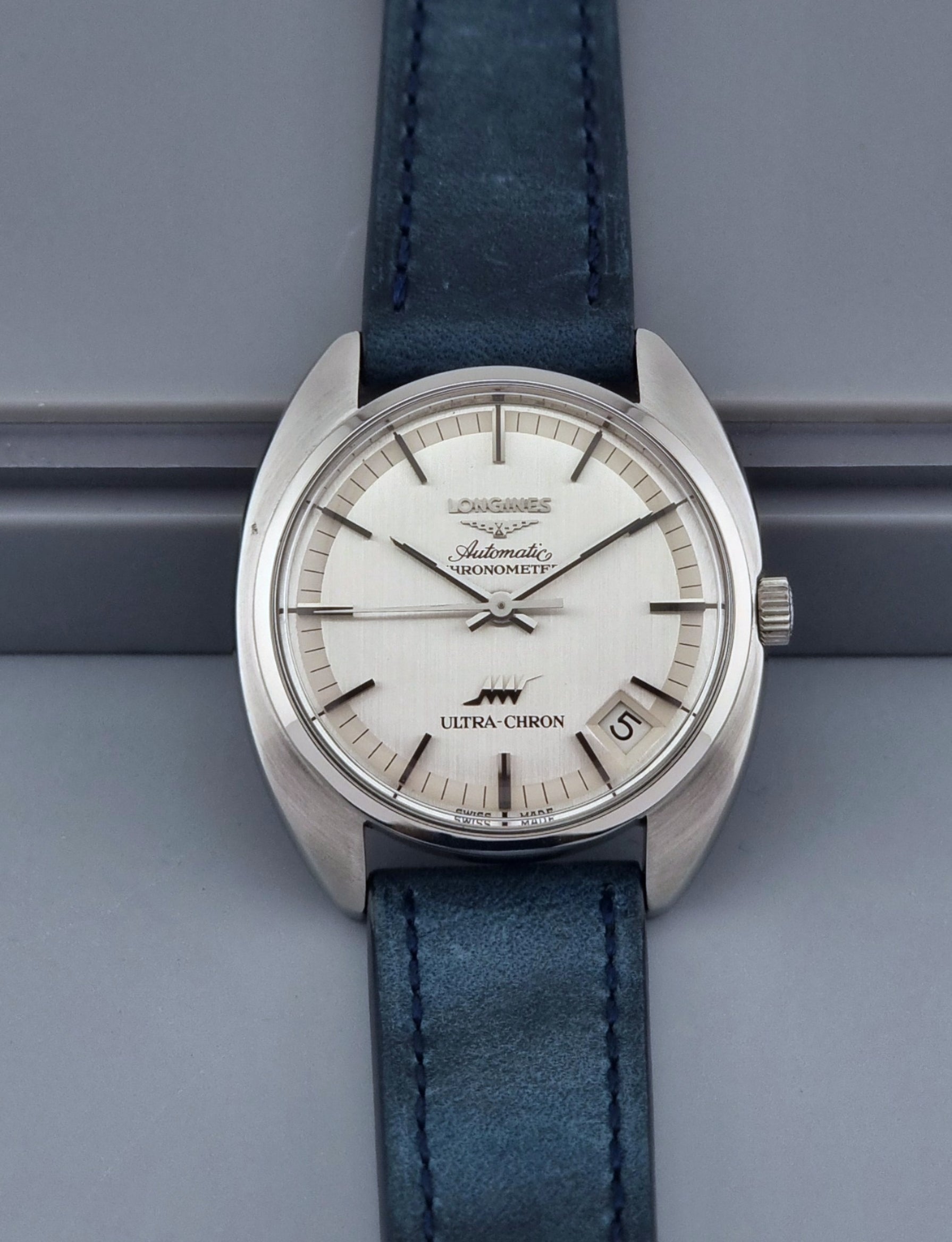 Vintage Longines Ultra-Chron wristwatch with blue strap and silver case on a gray background