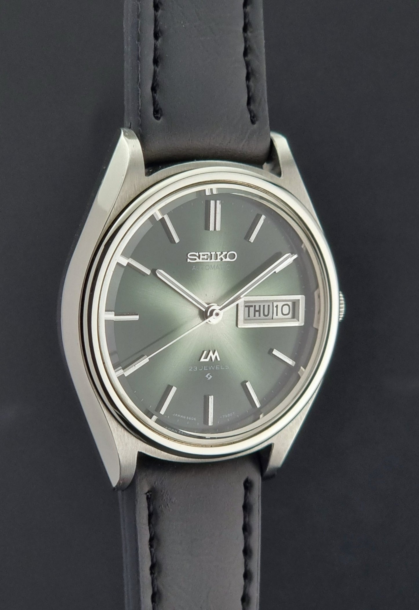 Seiko watch with a dark strap and green dial on a black background