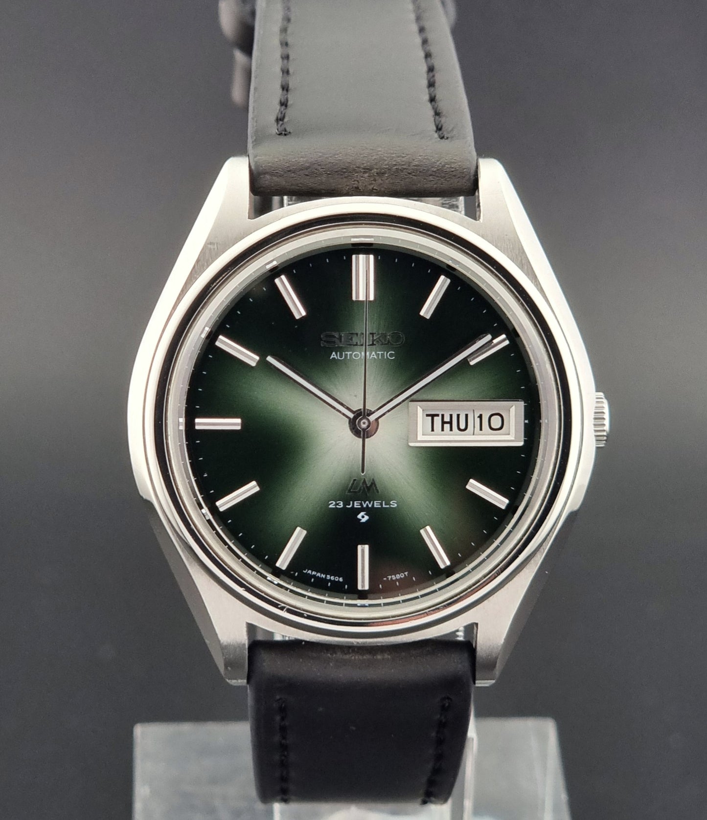 Wristwatch with black leather strap and green gradient dial on a gray background