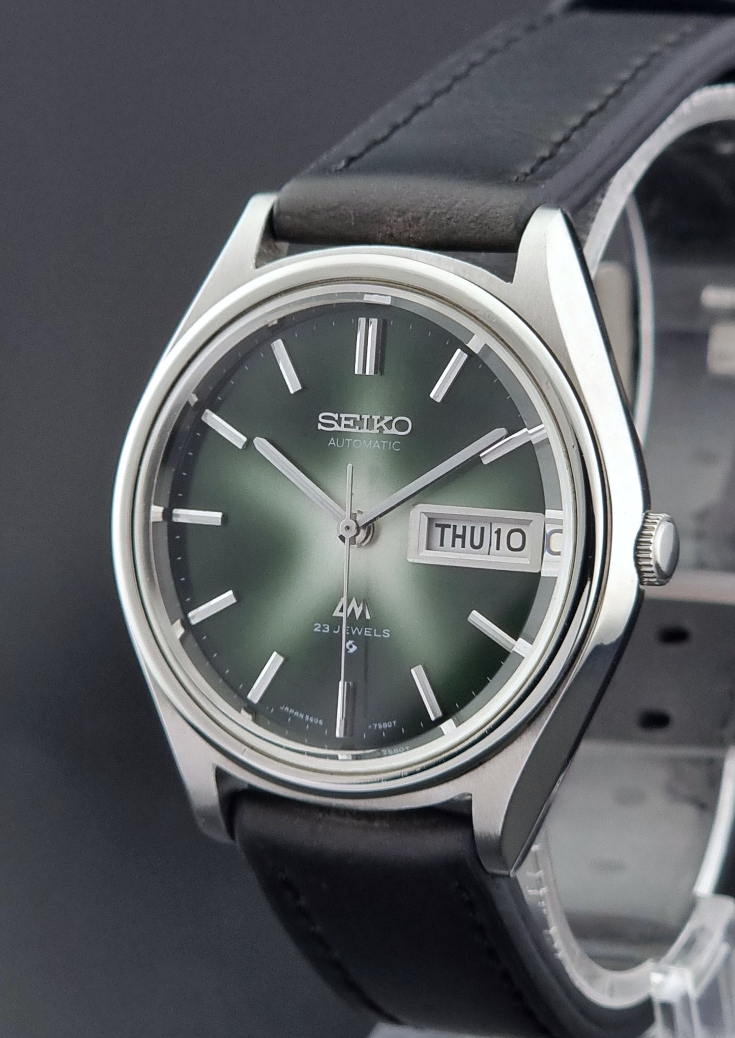 Seiko watch with green face and black leather strap on a dark background