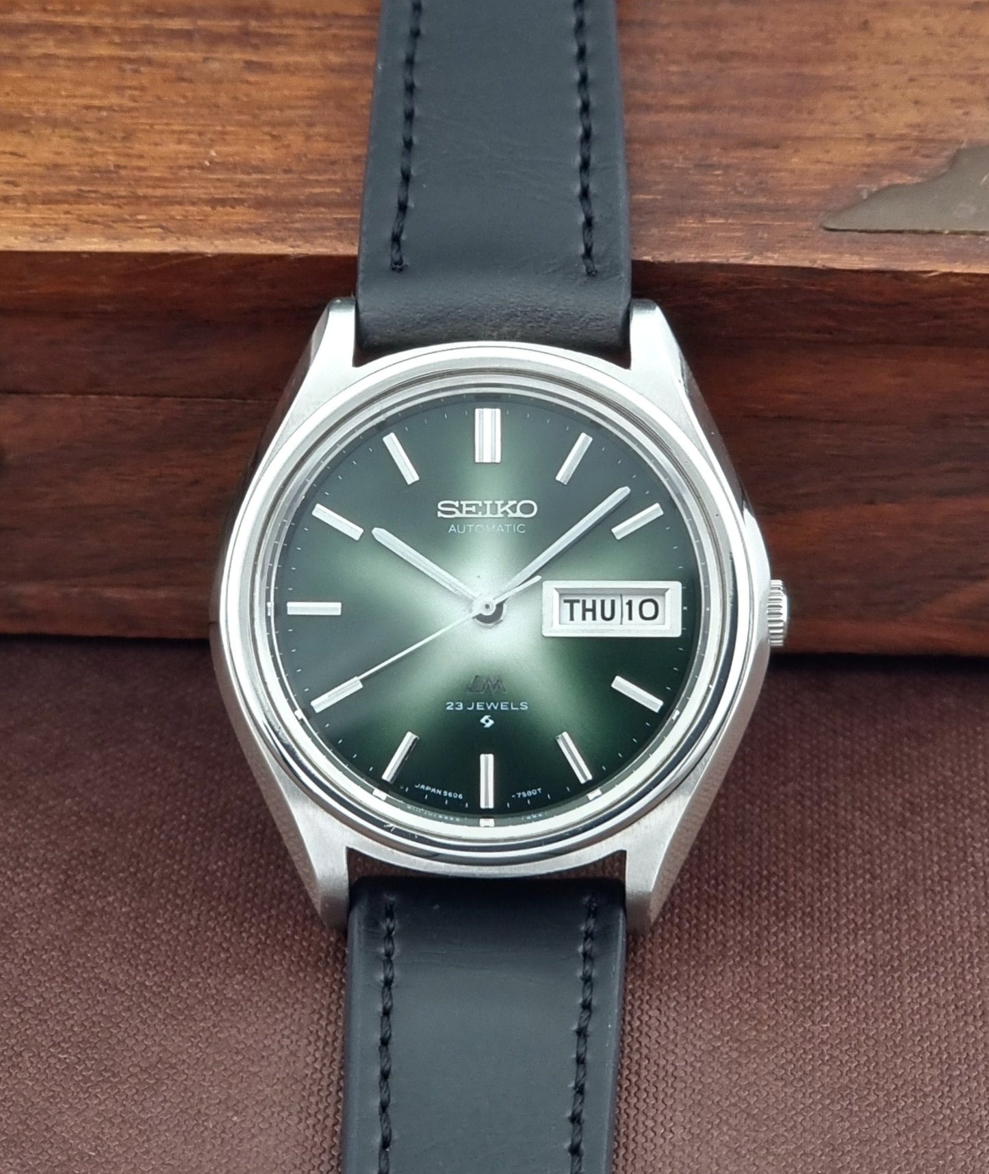 Seiko watch with green face and black leather strap on wooden surface