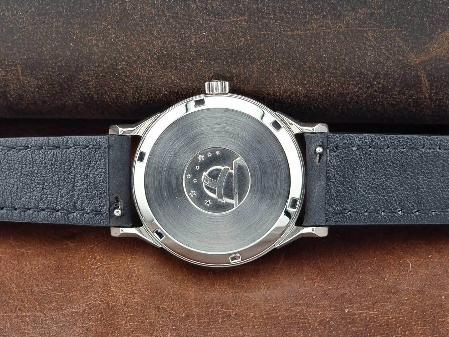 Omega Constellation watch case back with black leather strap on a brown leather background