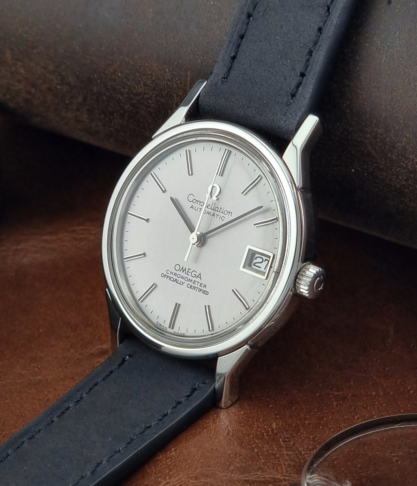 Omega watch with a silver dial and black leather strap on a brown surface