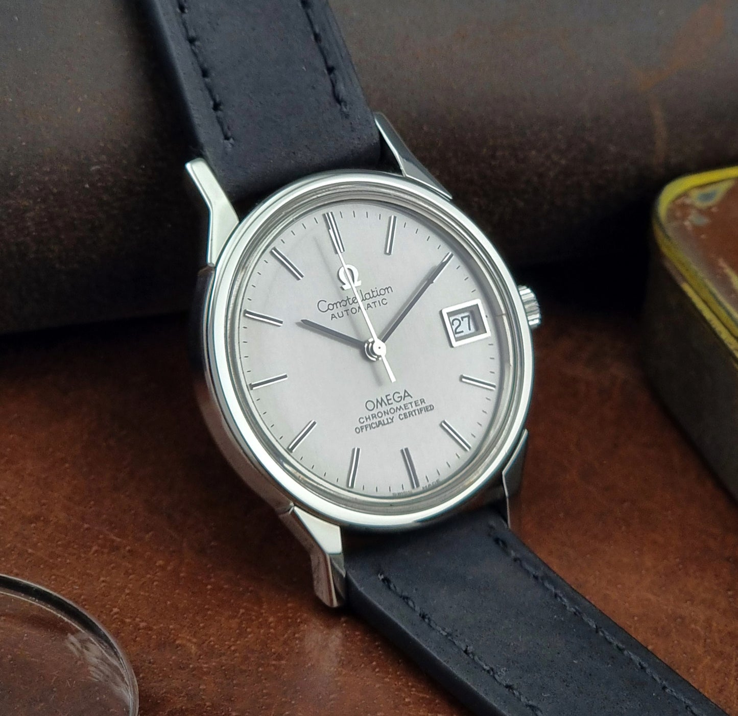 Omega watch with a silver dial and black leather strap on a brown surface