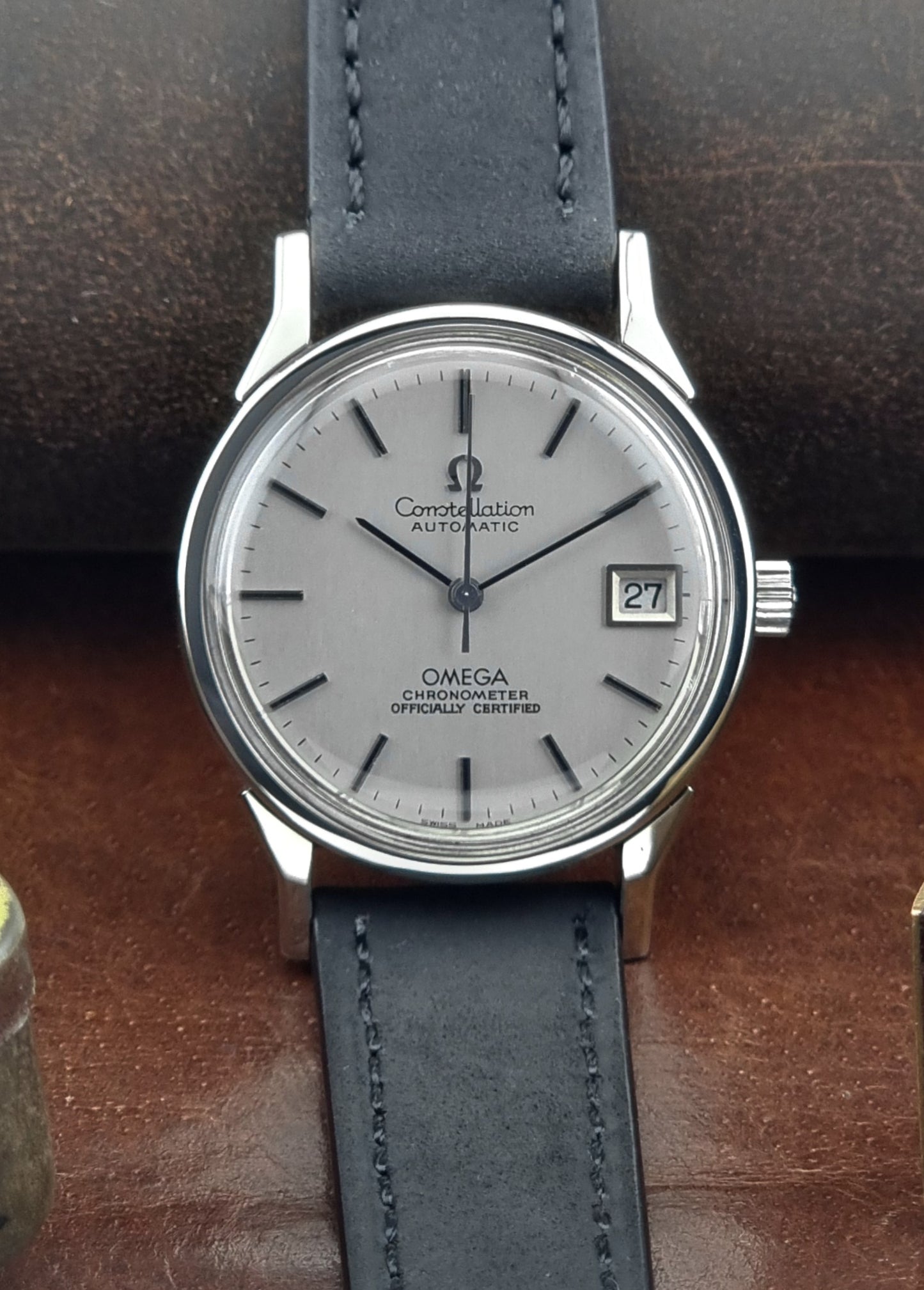 Omega watch with a silver case and black leather strap on a brown surface