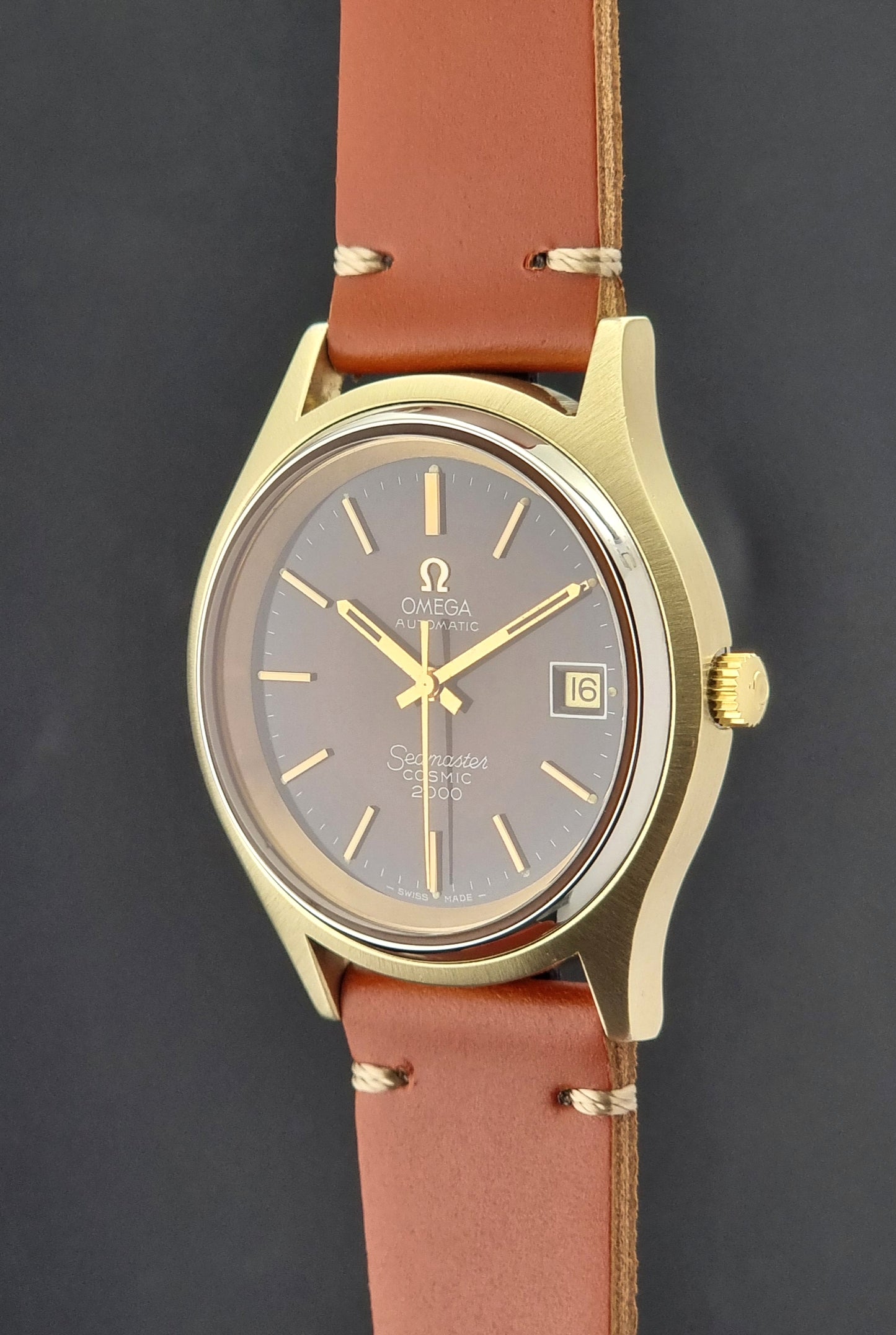 Crown side view of a Vintage Omega Seamaster Cosmic 2000Gold watch with brown leather strap on a dark background