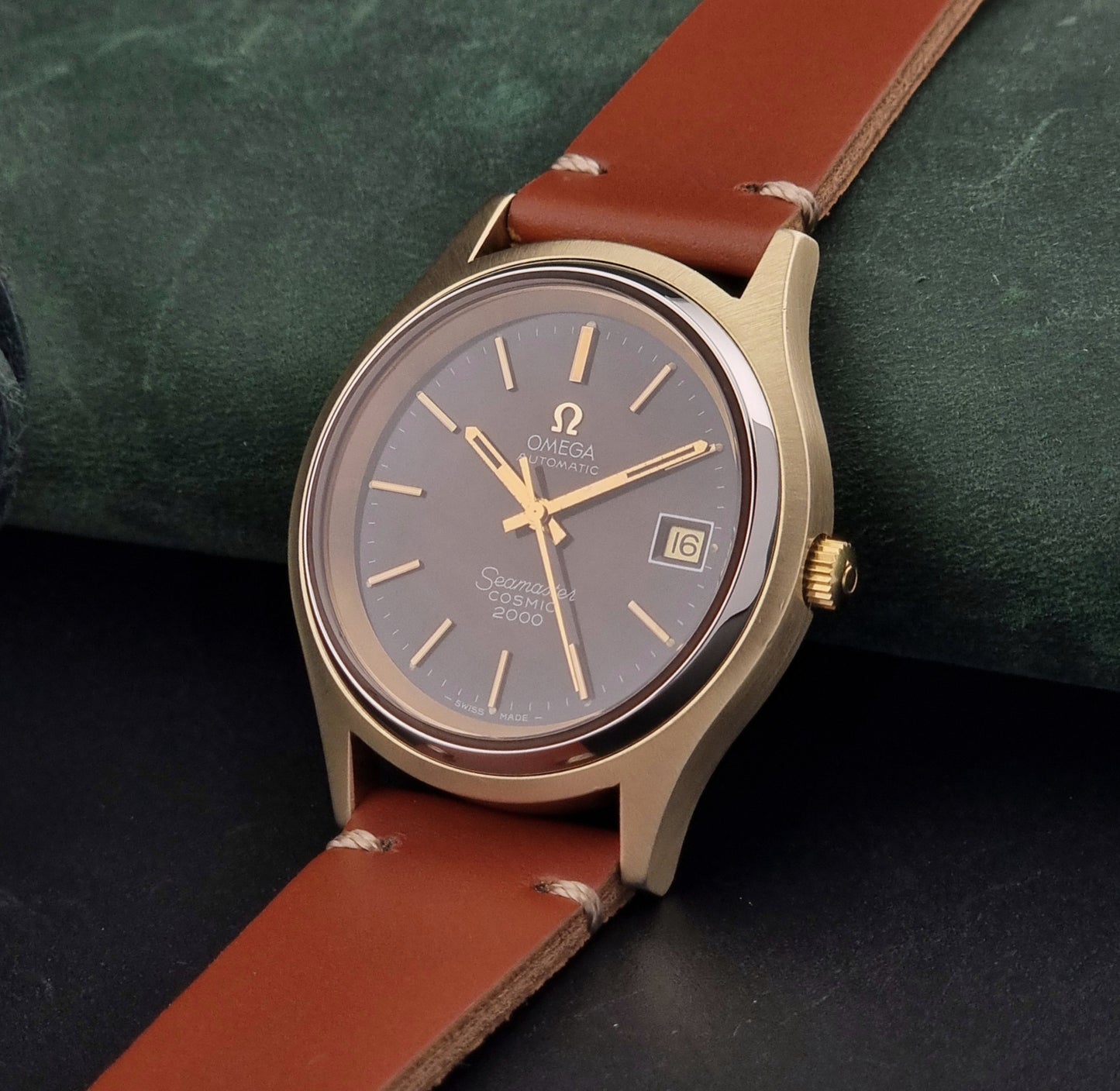 Vintage Omega Seamaster Cosmic 2000 watch with brown leather strap on a dark green background