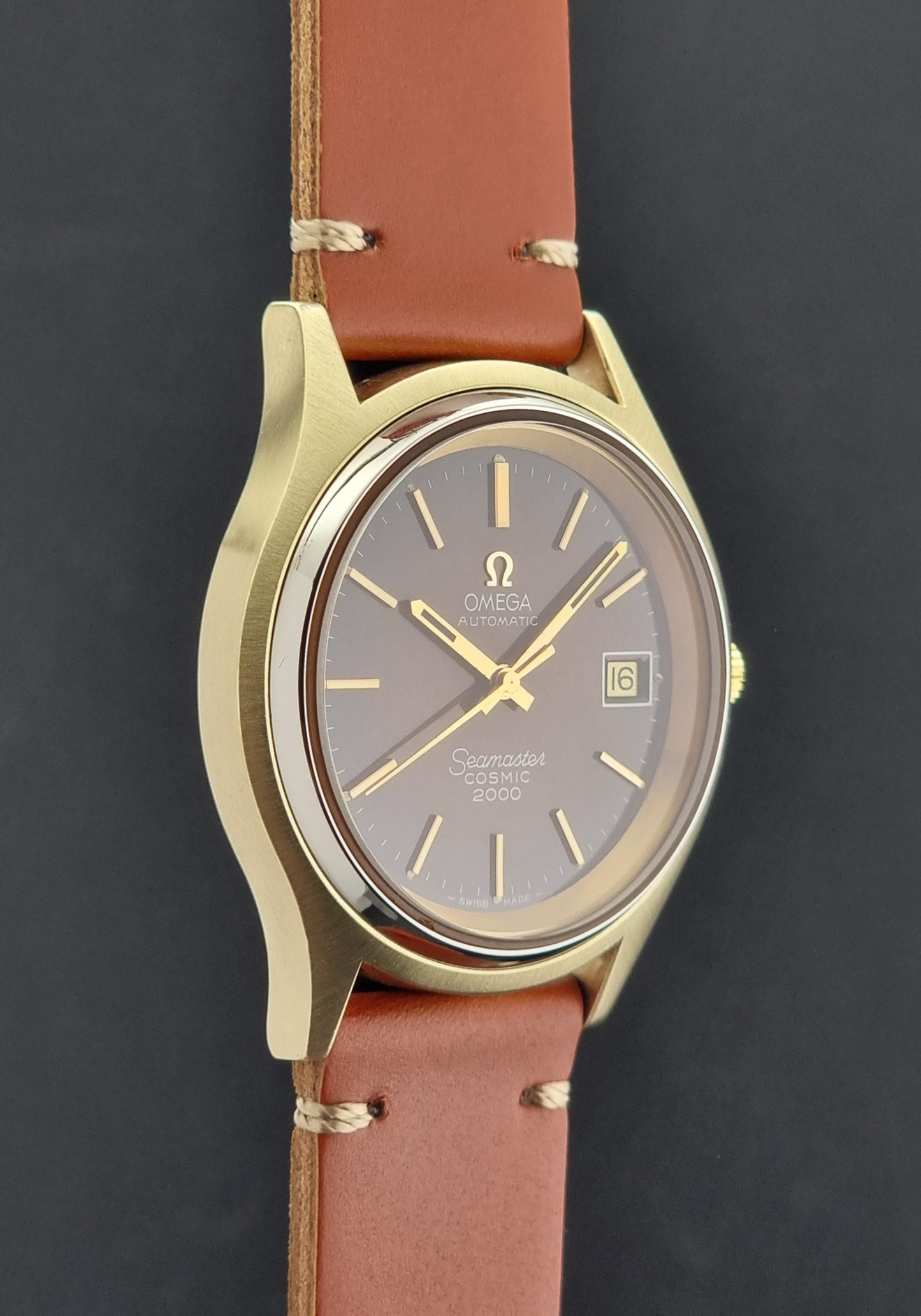 Side view of a Vintage Omega Seamaster Cosmic 2000 Gold watch with brown leather strap on a dark background