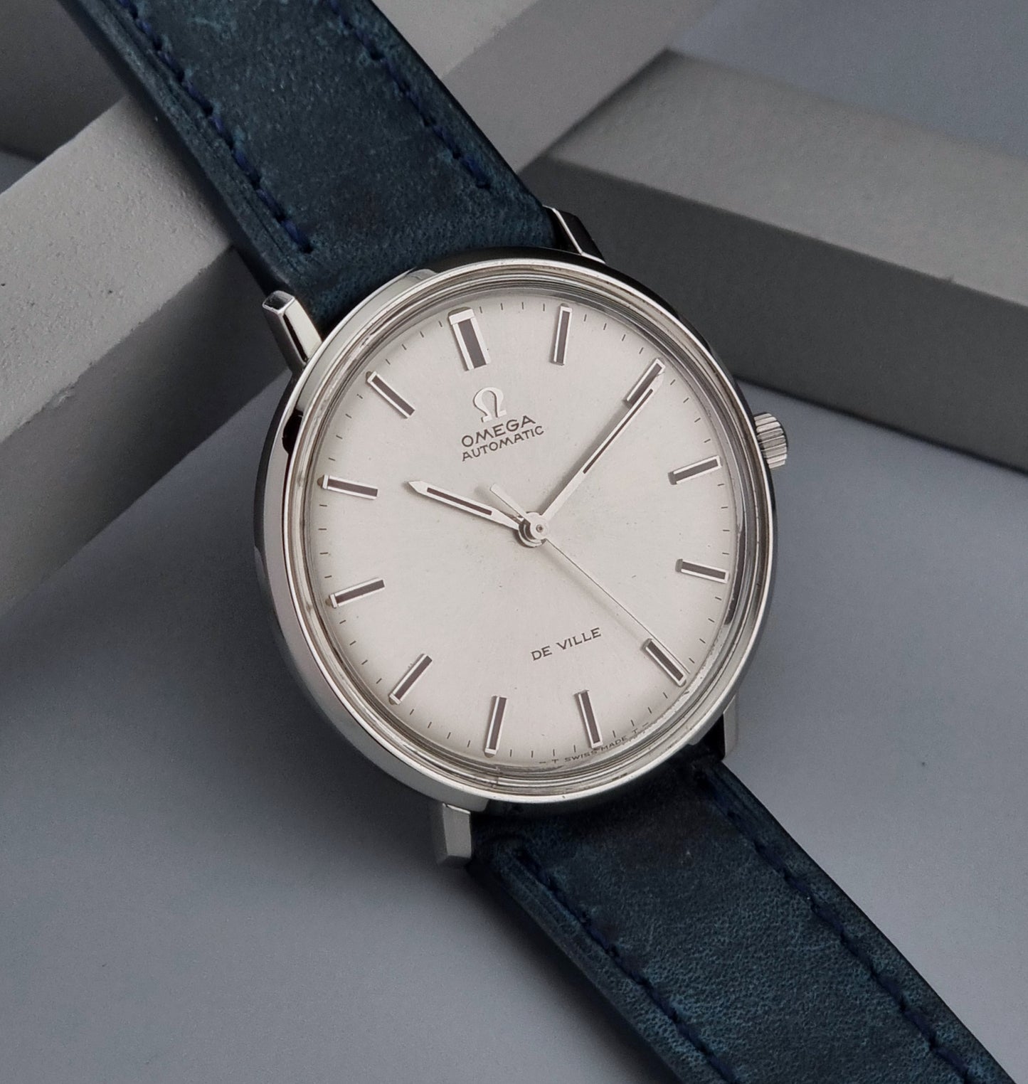 Vintage Omega De-Ville watch with a blue leather strap on a gray surface