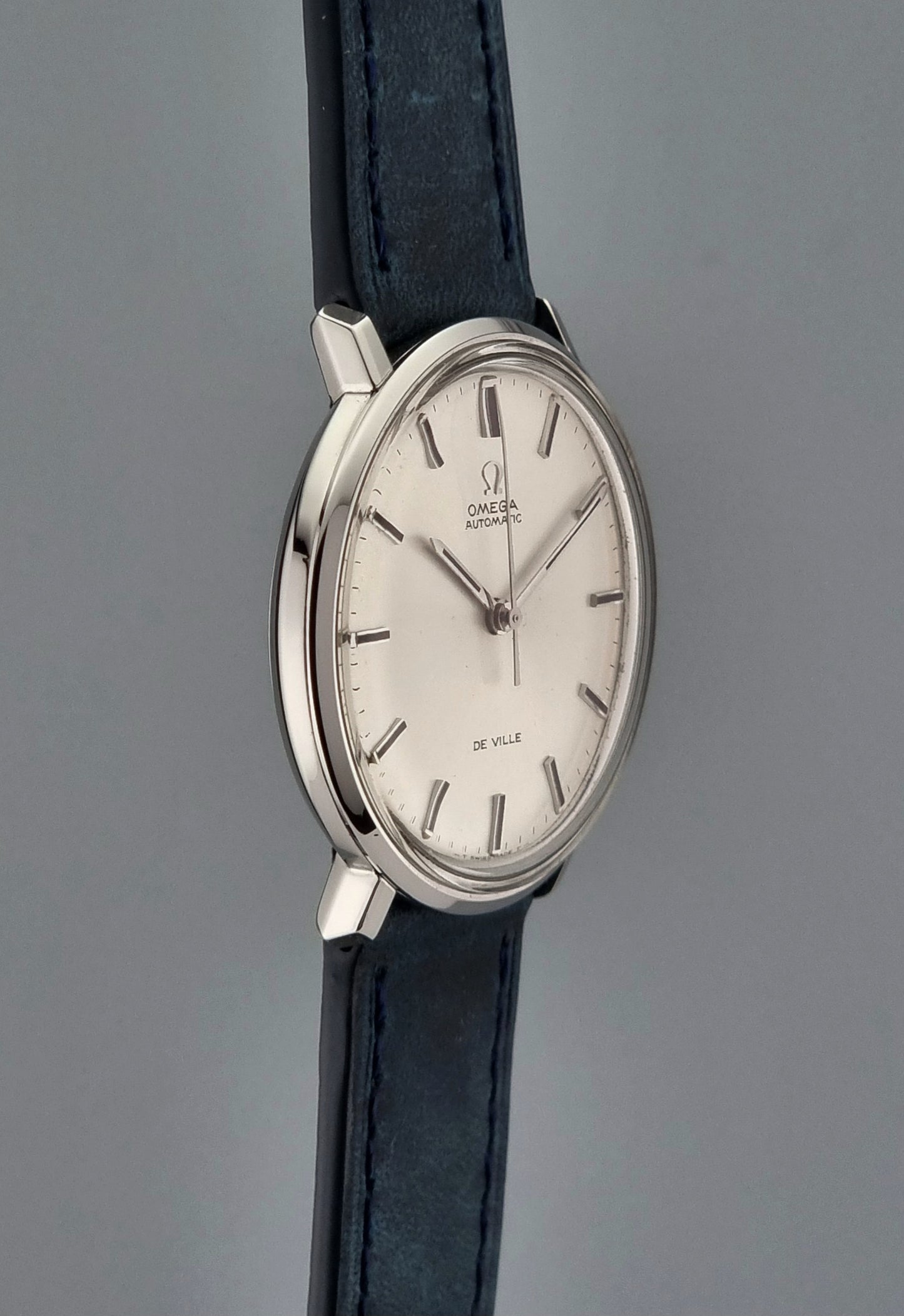 Vintage Omega De-Ville Wristwatch with silver case and black leather strap on a gray background