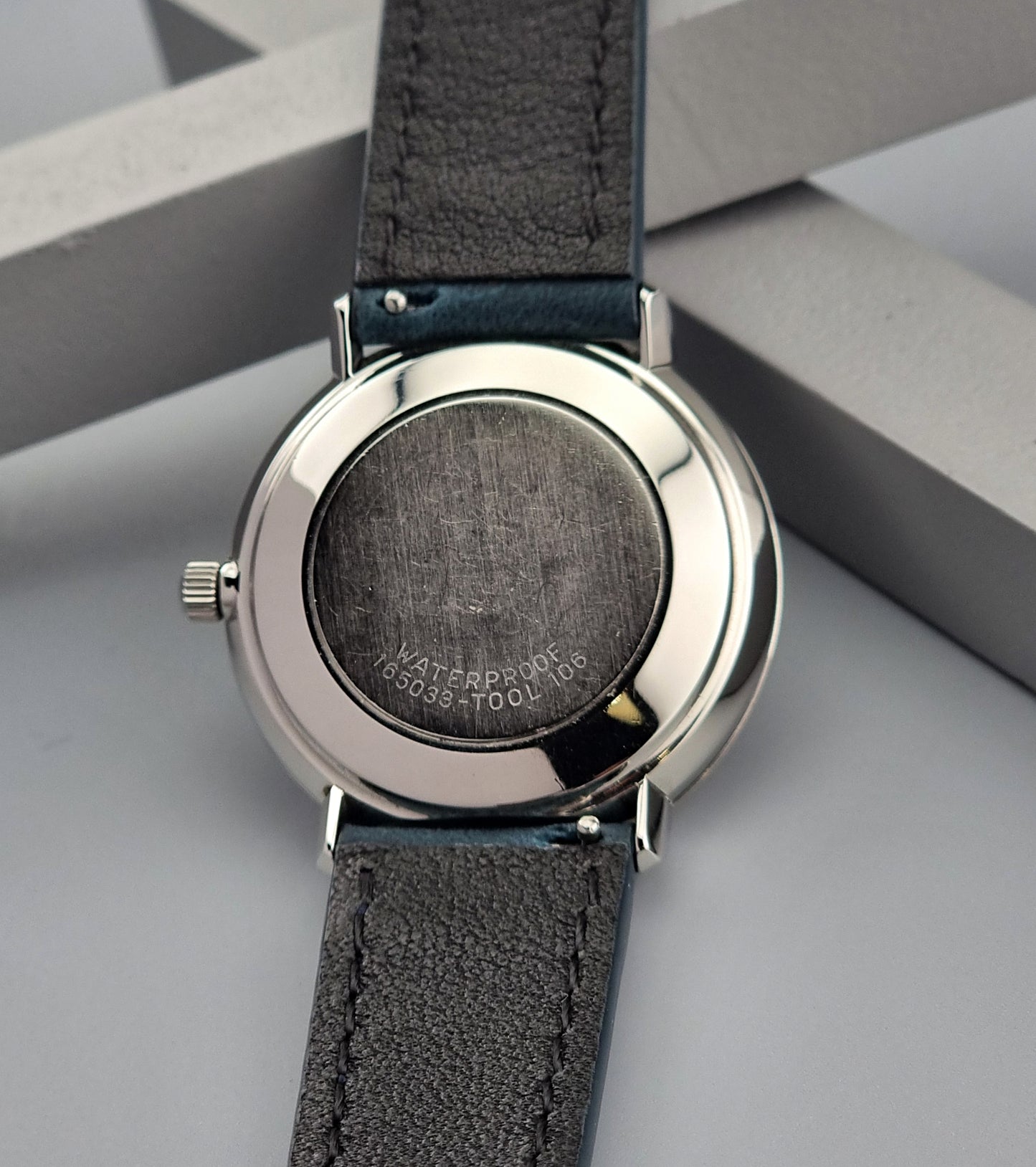 Wristwatch case back with dark leather strap and silver case on a light gray background
