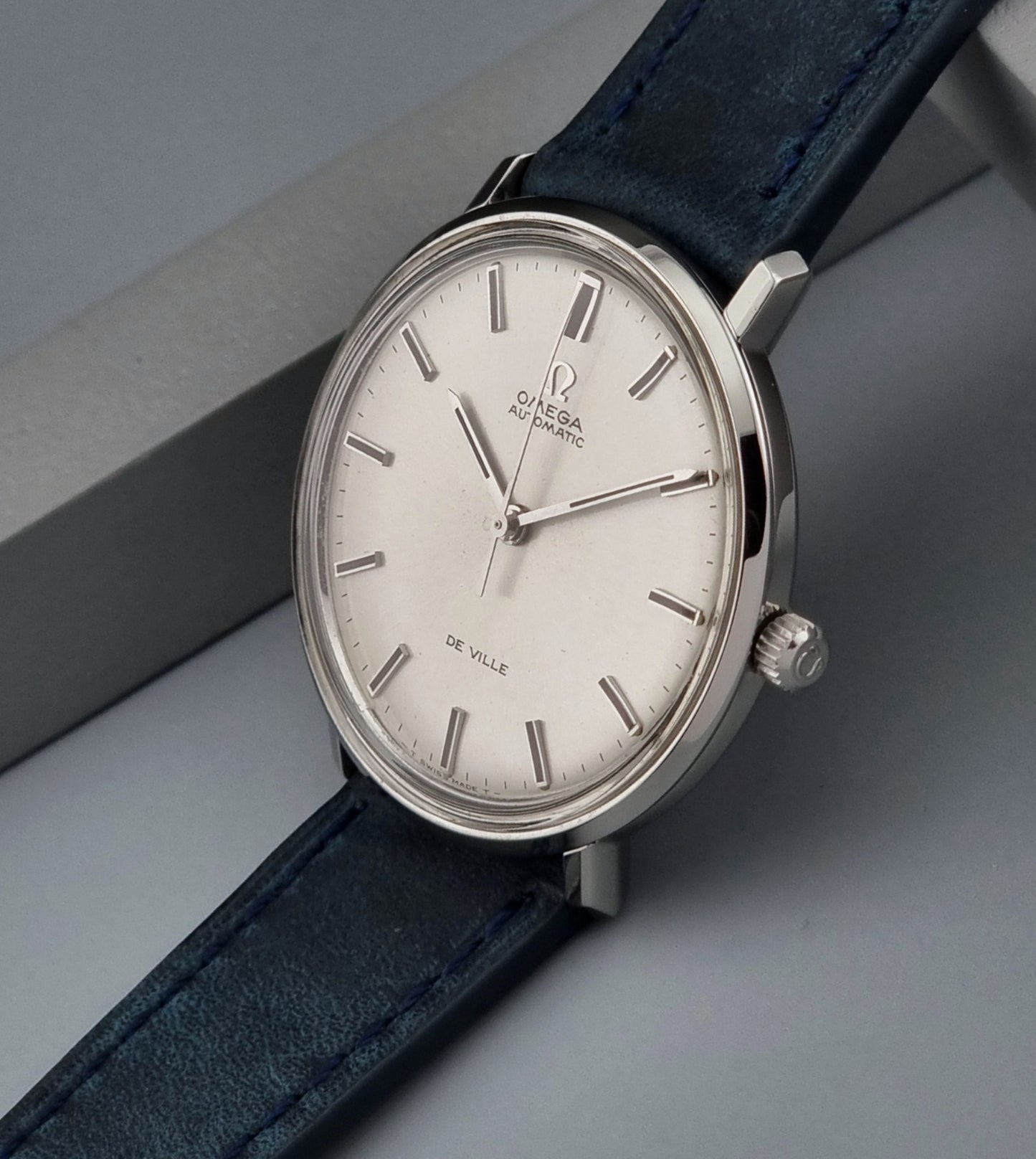 Vintage Omega De-Ville watch with silver dial and blue leather strap on a gray background