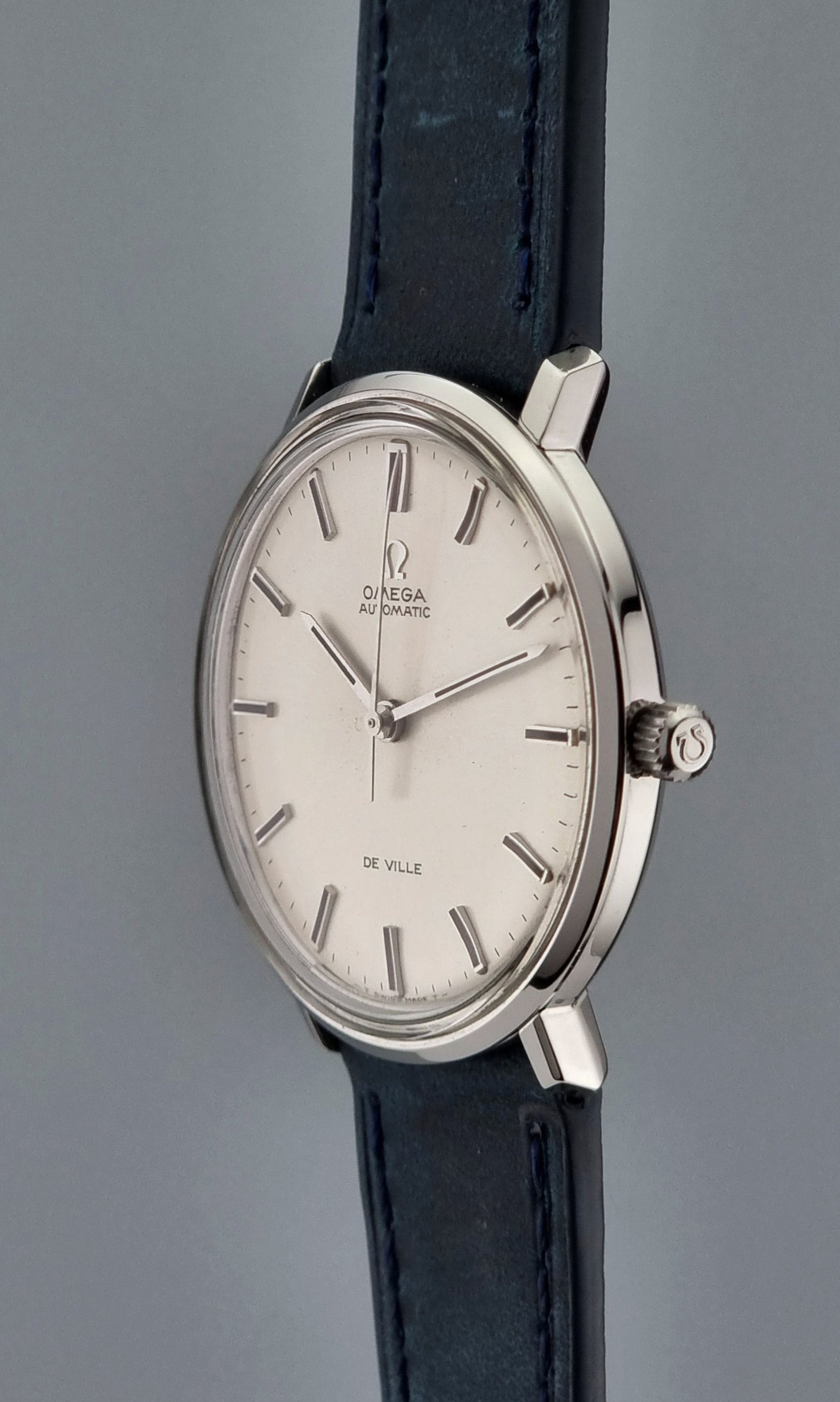 Vintage Omega De-Ville watch with a silver case and black leather strap on a gray background