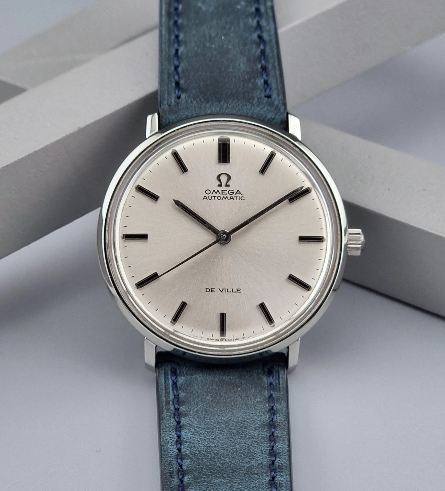 Vintage Omega De-Ville watch with blue leather strap on a gray background