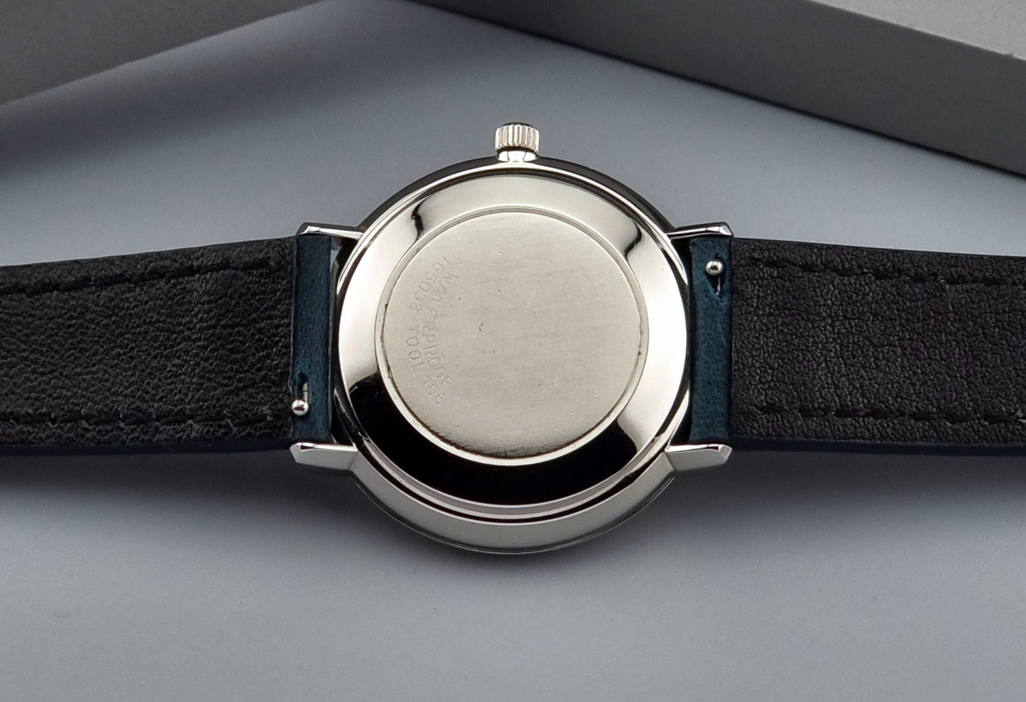Close-up of a Vintage Omega De-Ville case back with a black leather strap on a gray background