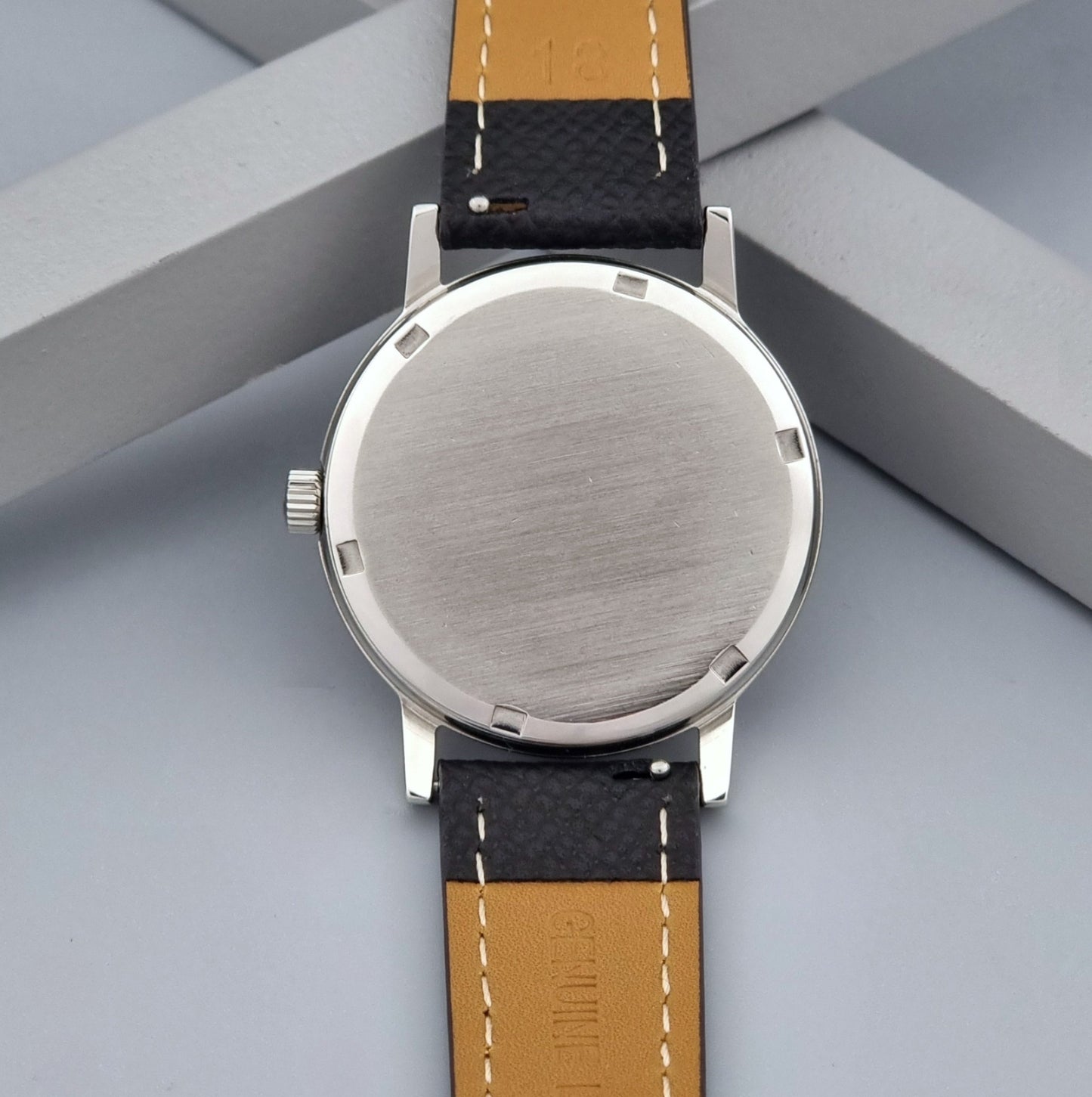 Vintage Omega Geneve 136.0098 Wristwatch with black strap and silver case on a gray background case back view