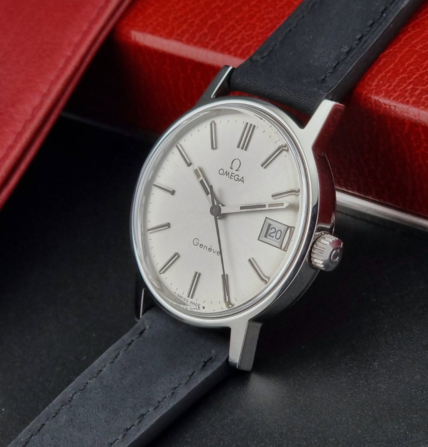 Vintage Omega Geneve watch with black leather strap on a dark surface with red background